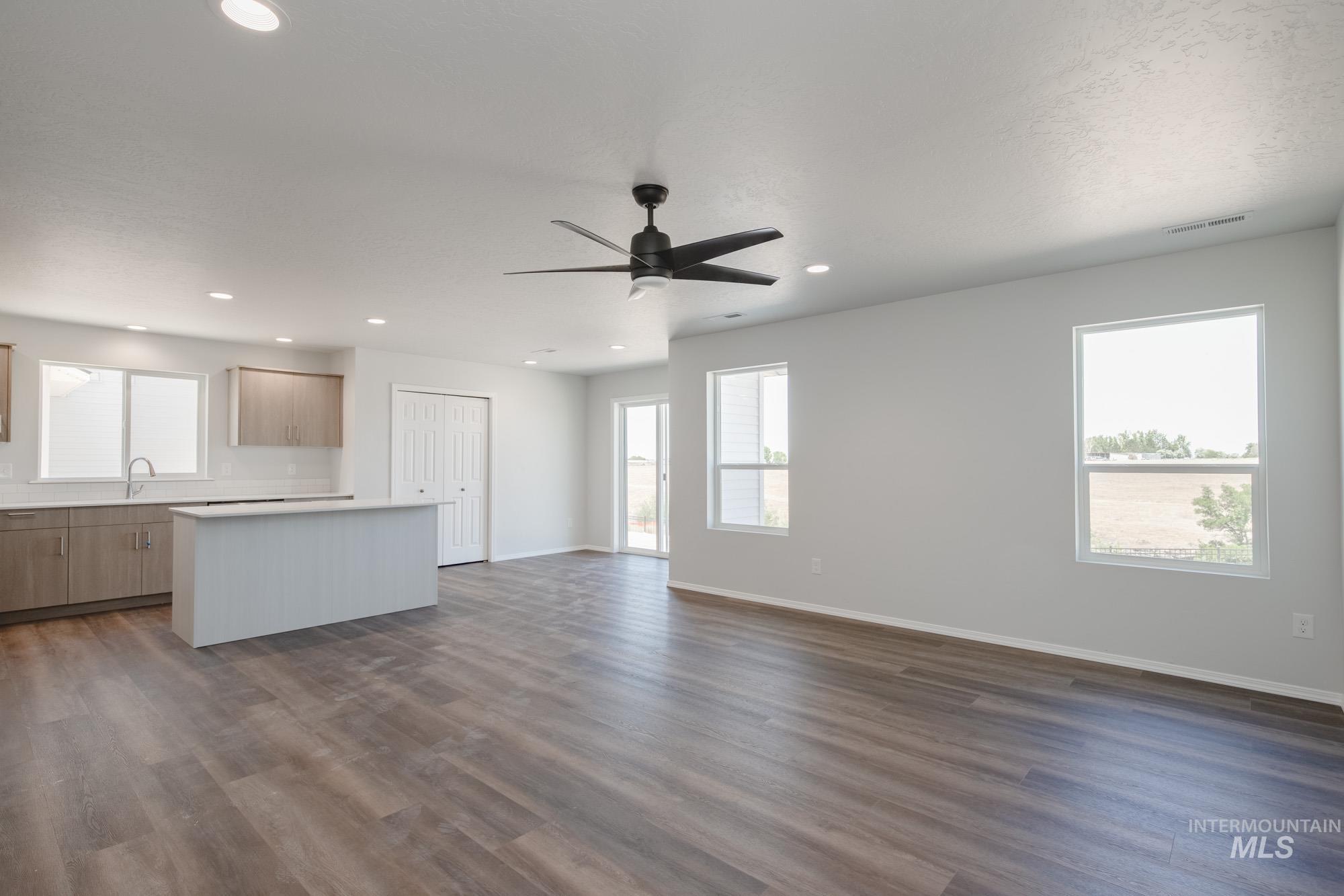 Kitchen with open floor plan, a kitchen island, dark wood-type flooring, light countertops, and a ceiling fan