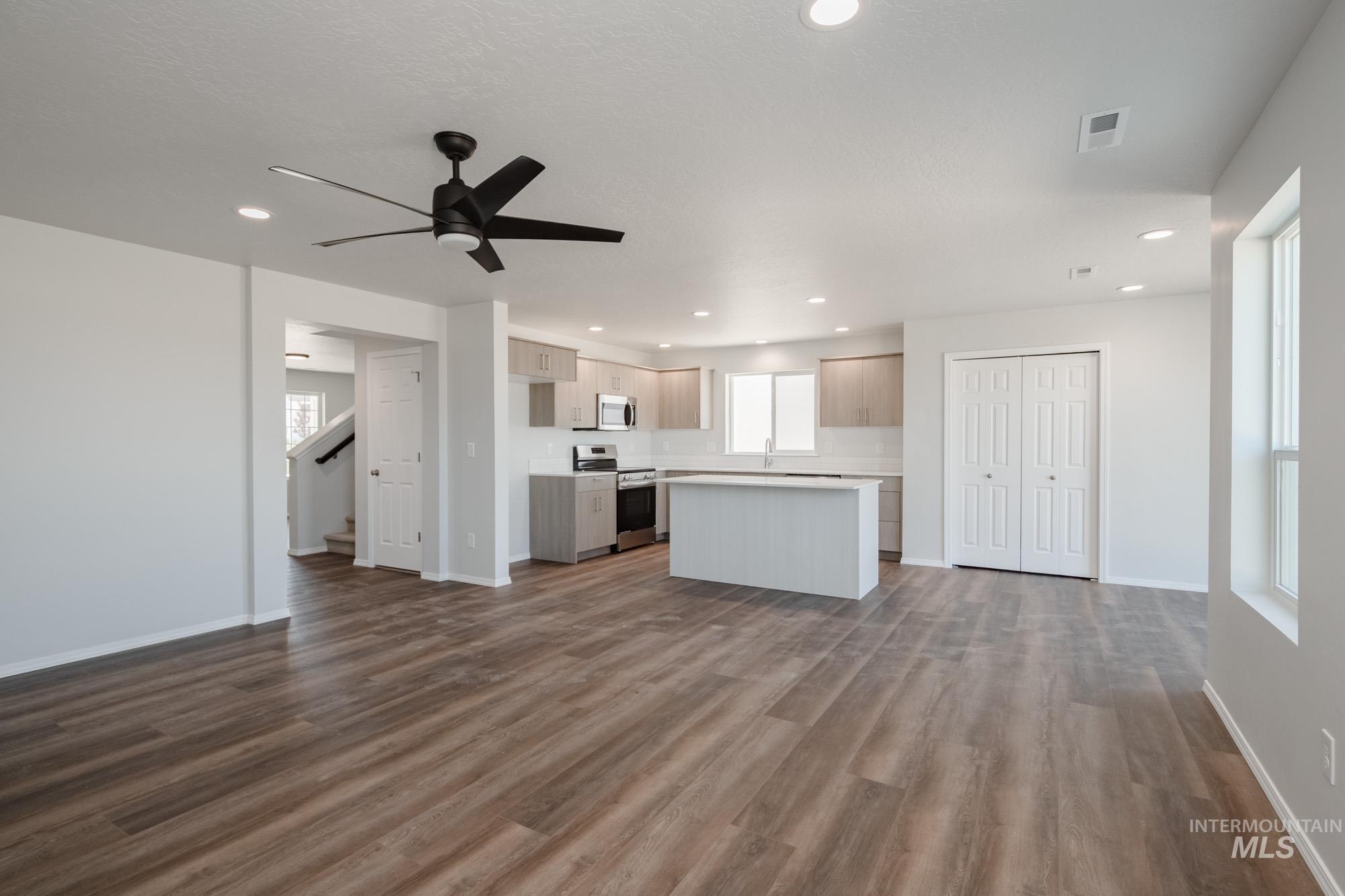 Unfurnished living room featuring dark wood-type flooring, a ceiling fan, recessed lighting, and stairs