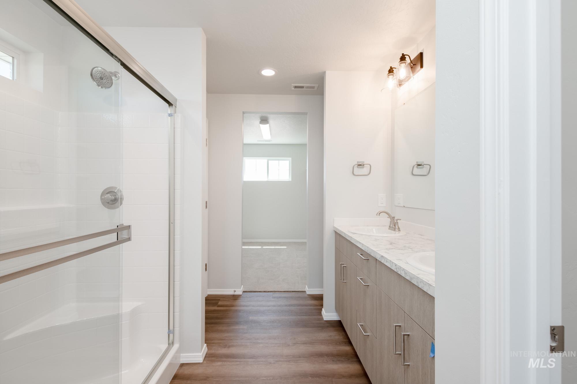 Full bath with double vanity, a shower stall, wood finished floors, and recessed lighting