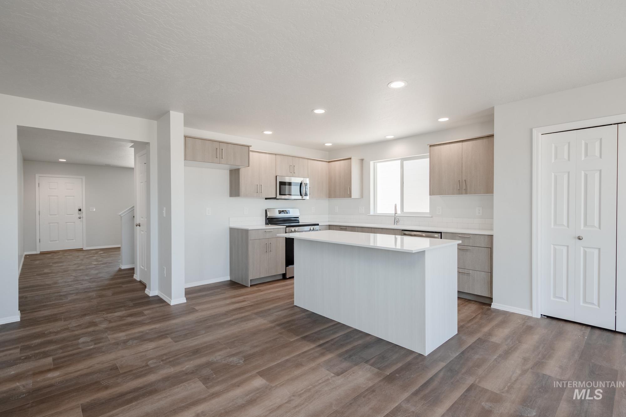 Kitchen with stainless steel appliances, light countertops, dark wood finished floors, a center island, and recessed lighting
