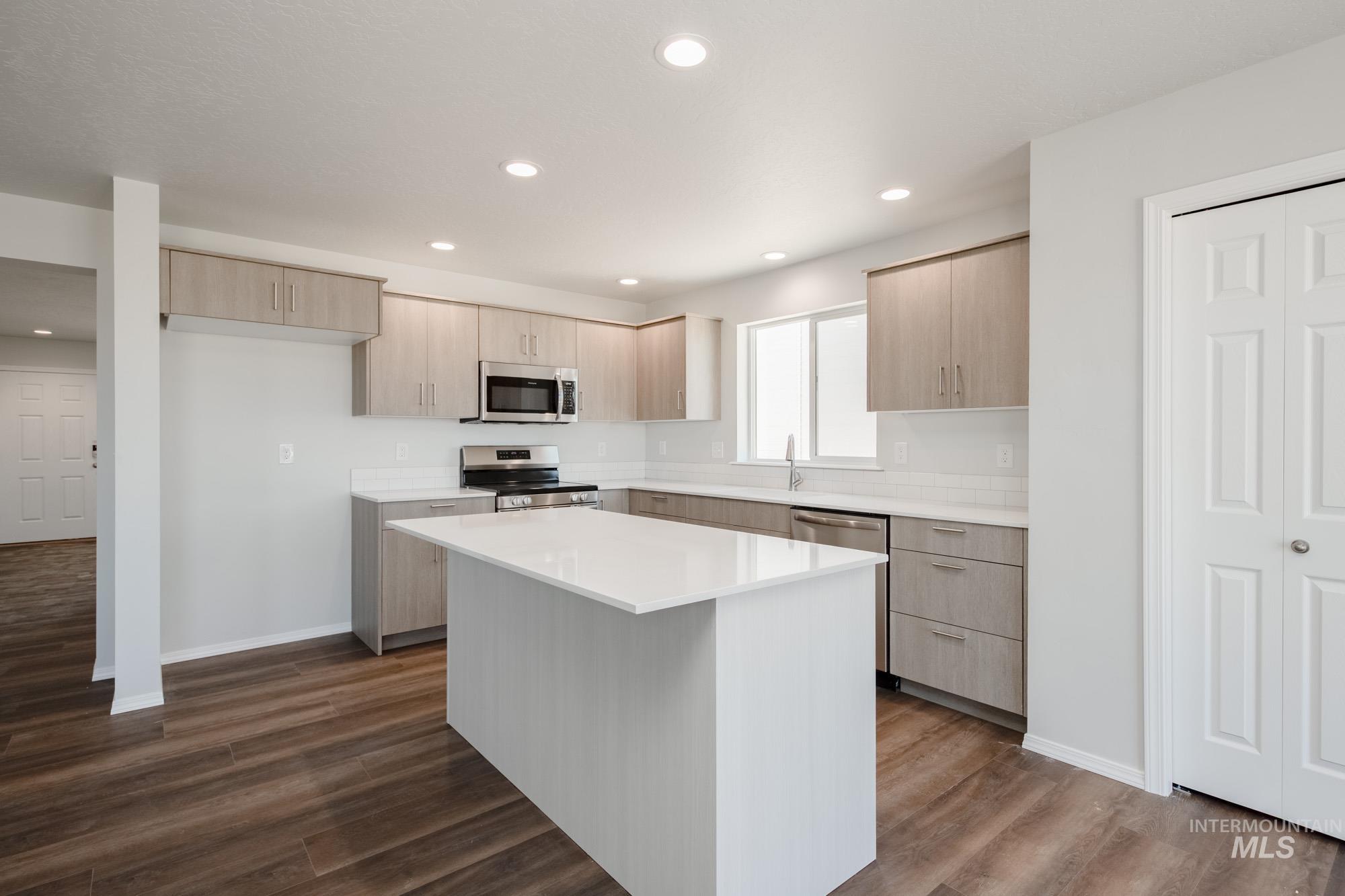 Kitchen with appliances with stainless steel finishes, light countertops, light brown cabinets, a kitchen island, and dark wood finished floors