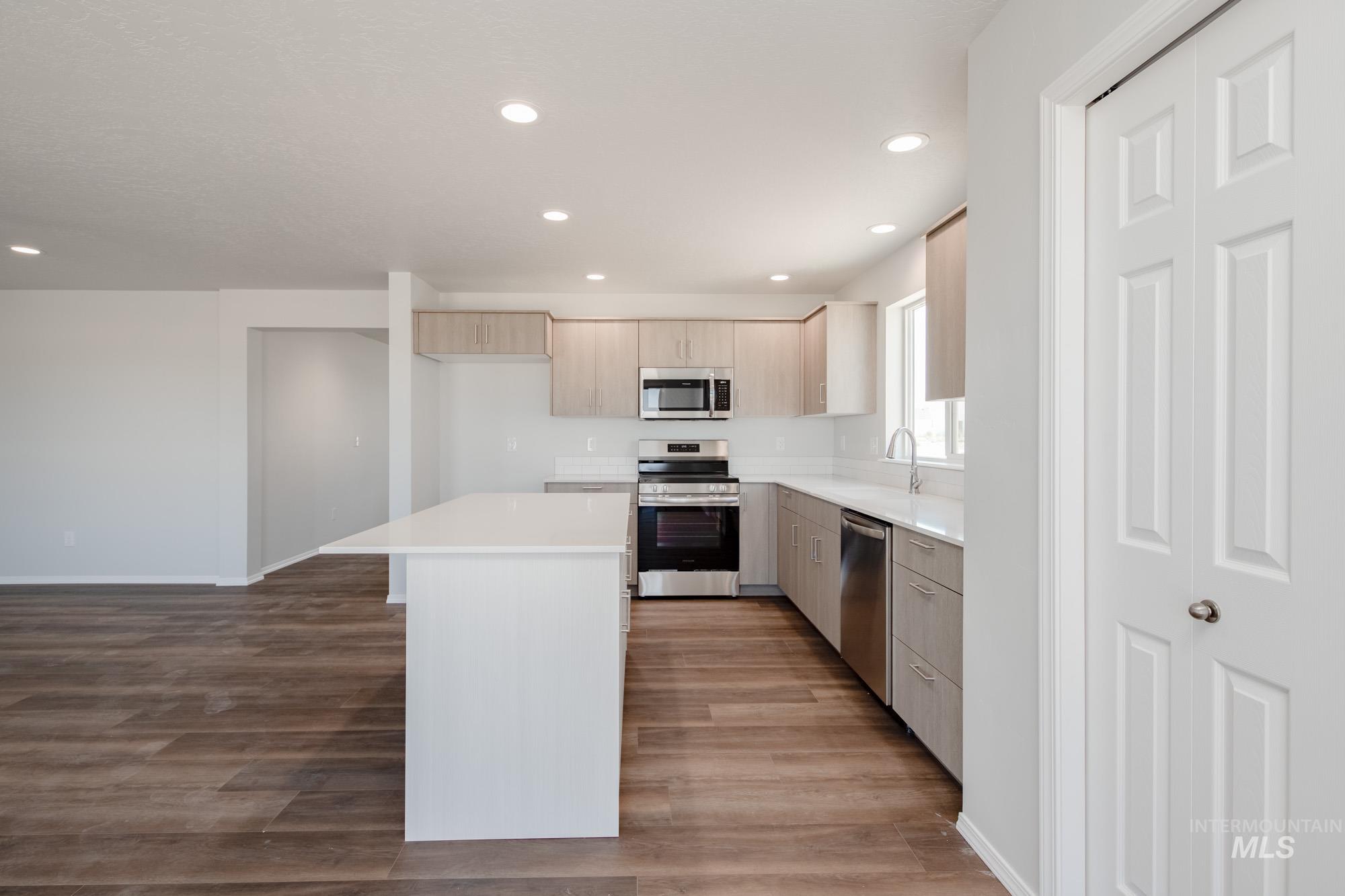 Kitchen featuring appliances with stainless steel finishes, wood finished floors, light countertops, a center island, and recessed lighting