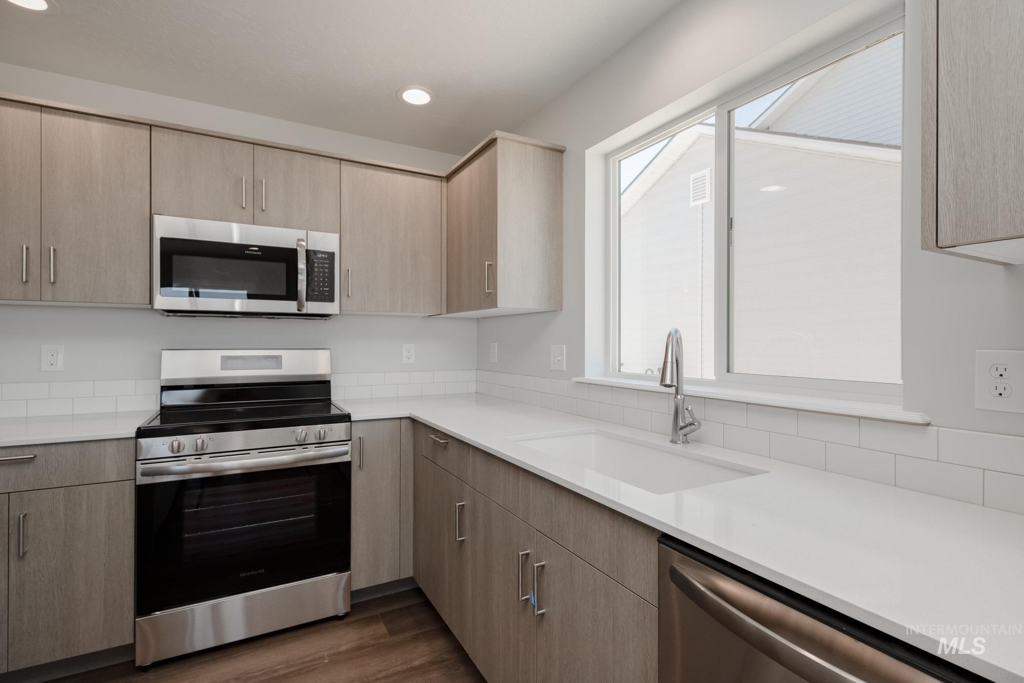 Kitchen featuring appliances with stainless steel finishes, light brown cabinetry, light countertops, recessed lighting, and dark wood-style floors