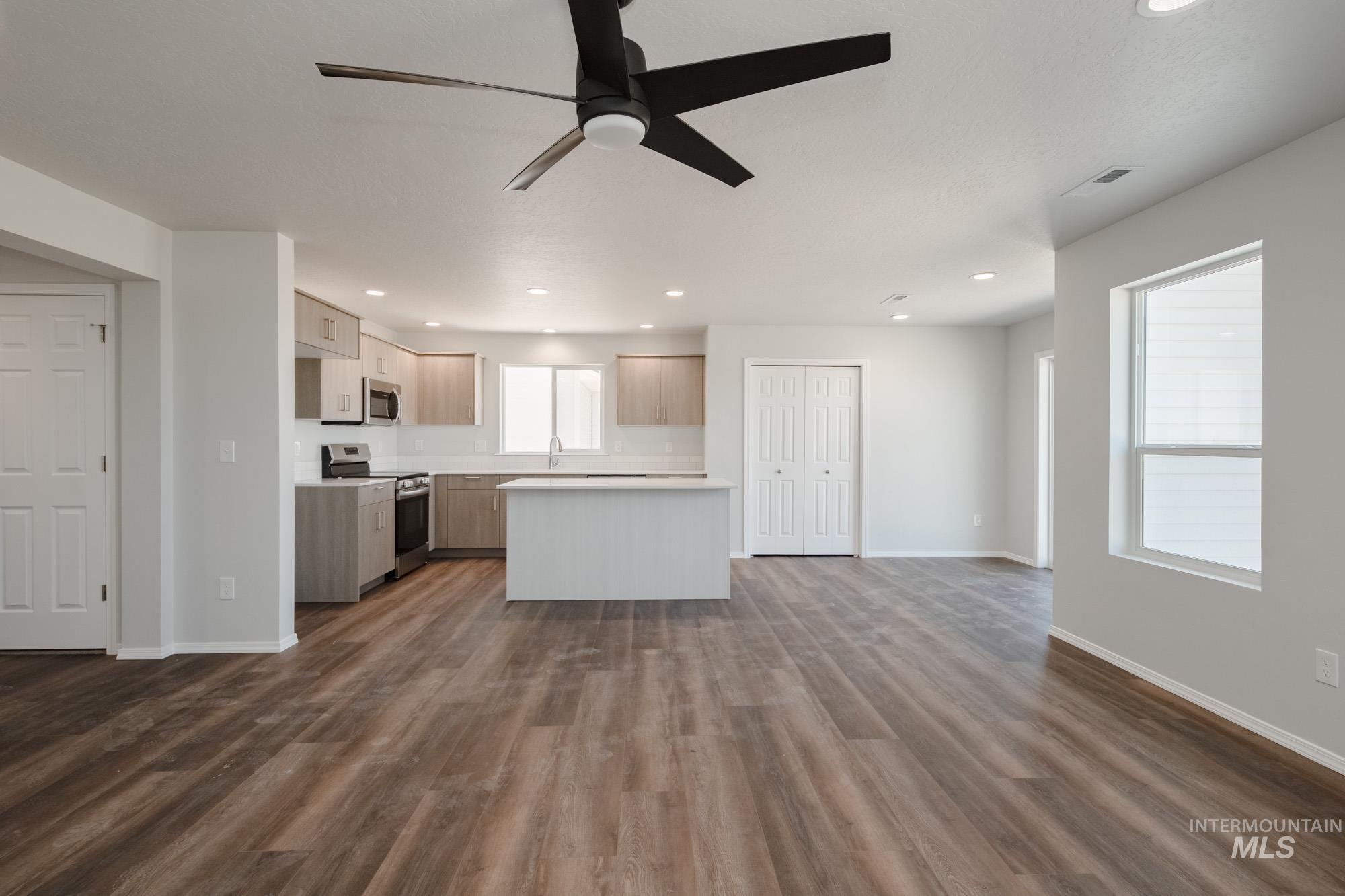 Kitchen featuring appliances with stainless steel finishes, open floor plan, ceiling fan, light countertops, and dark wood-style floors