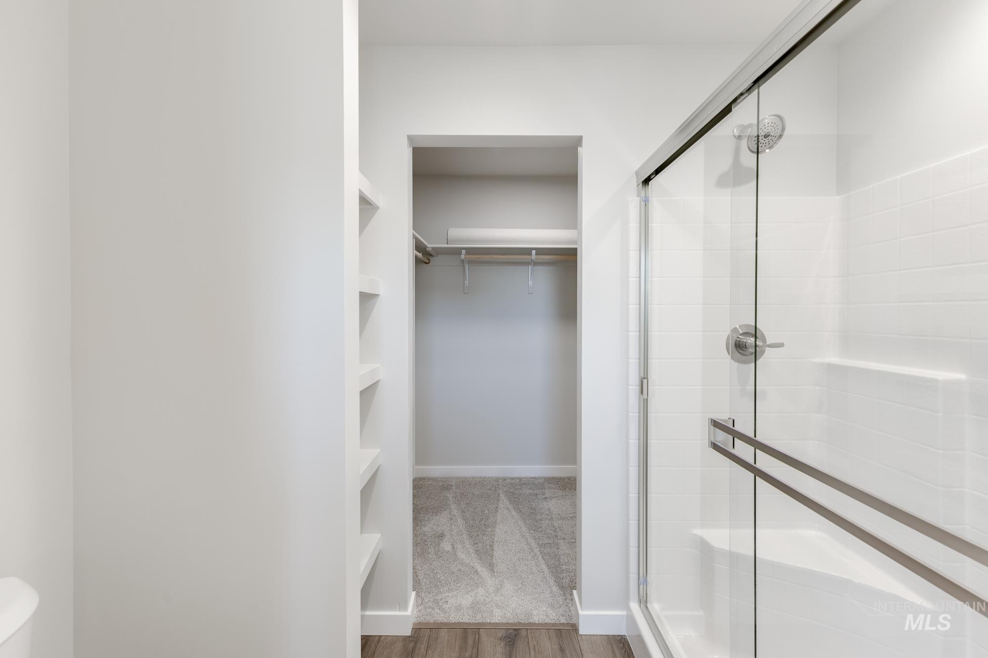 Full bathroom featuring a shower stall, a spacious closet, and wood finished floors
