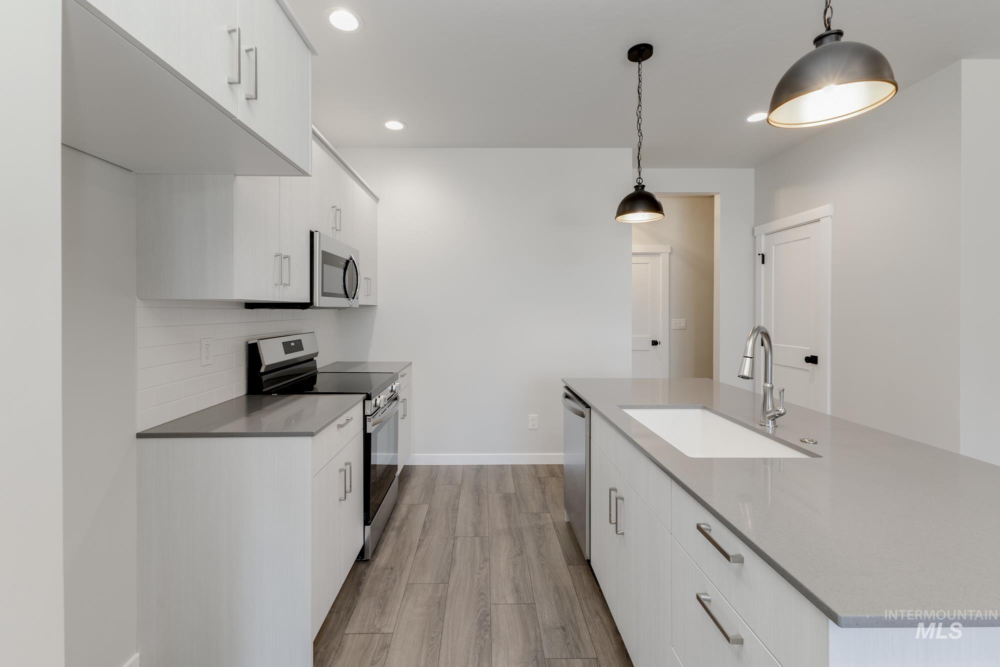 Kitchen with appliances with stainless steel finishes, white cabinetry, light wood-type flooring, and recessed lighting