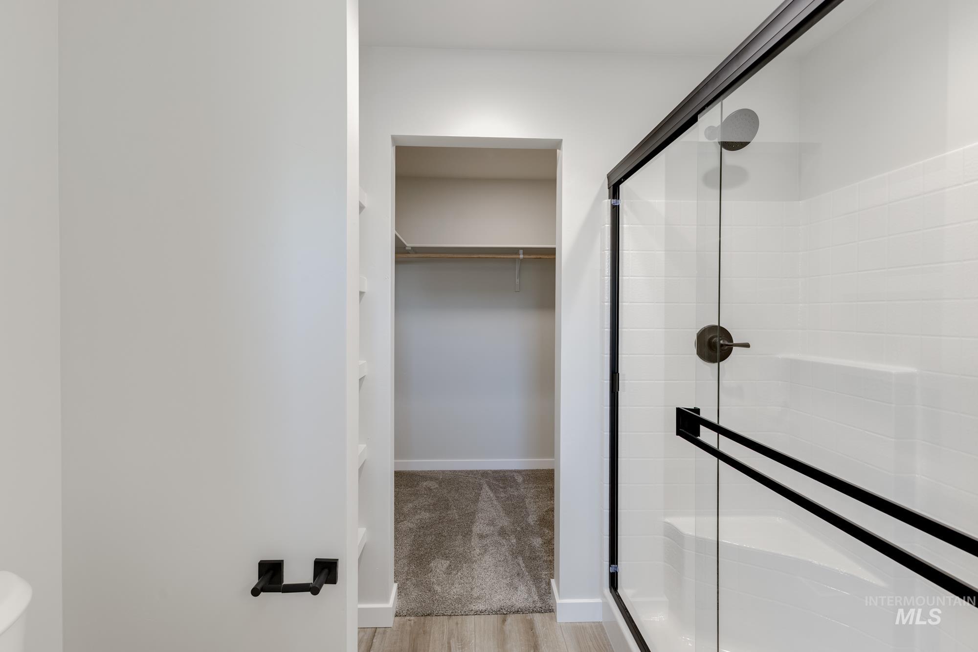 Full bathroom with a shower stall, a walk in closet, and wood finished floors