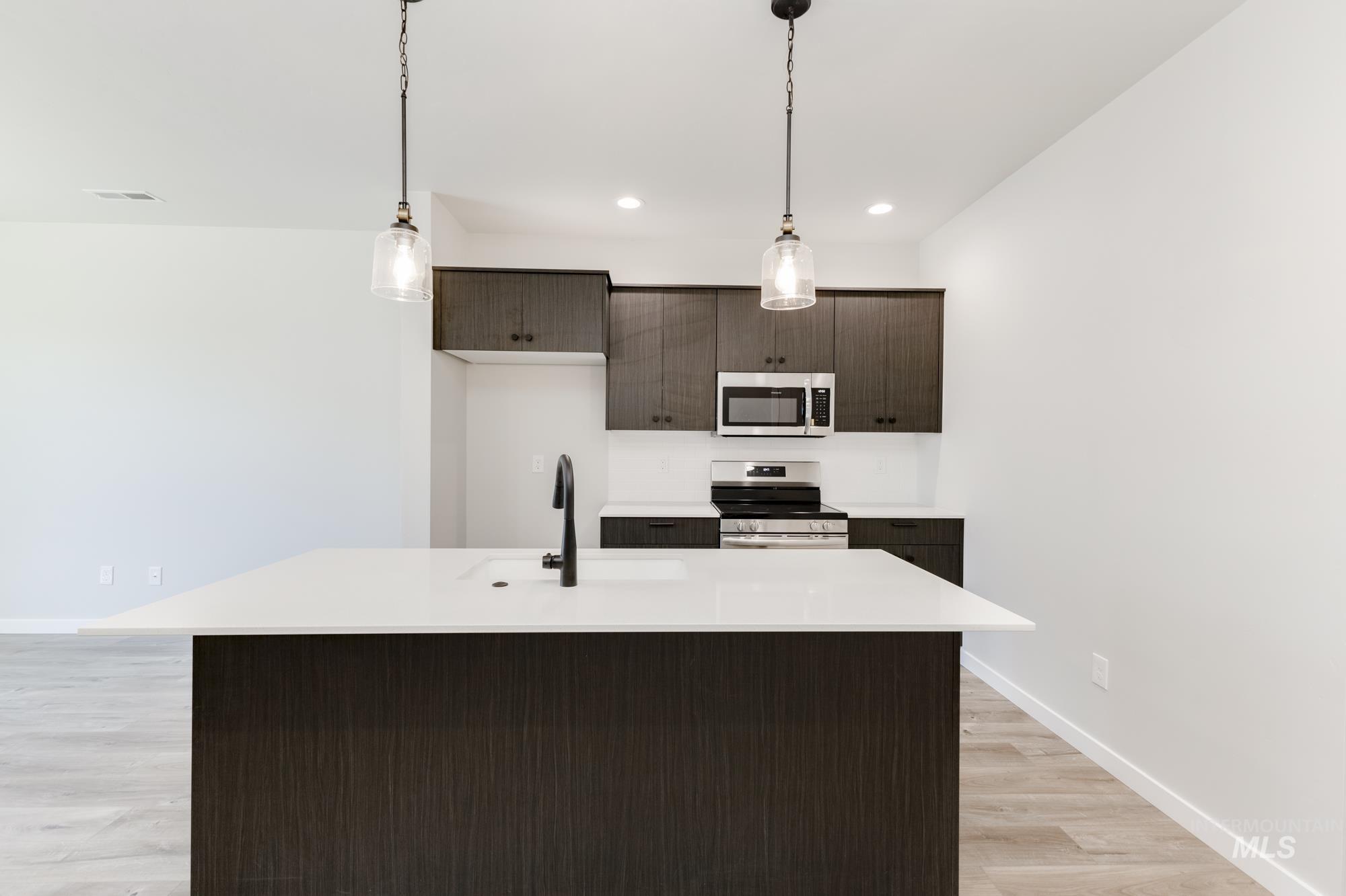 Kitchen with stainless steel appliances, light countertops, light wood-style floors, dark brown cabinetry, and decorative light fixtures