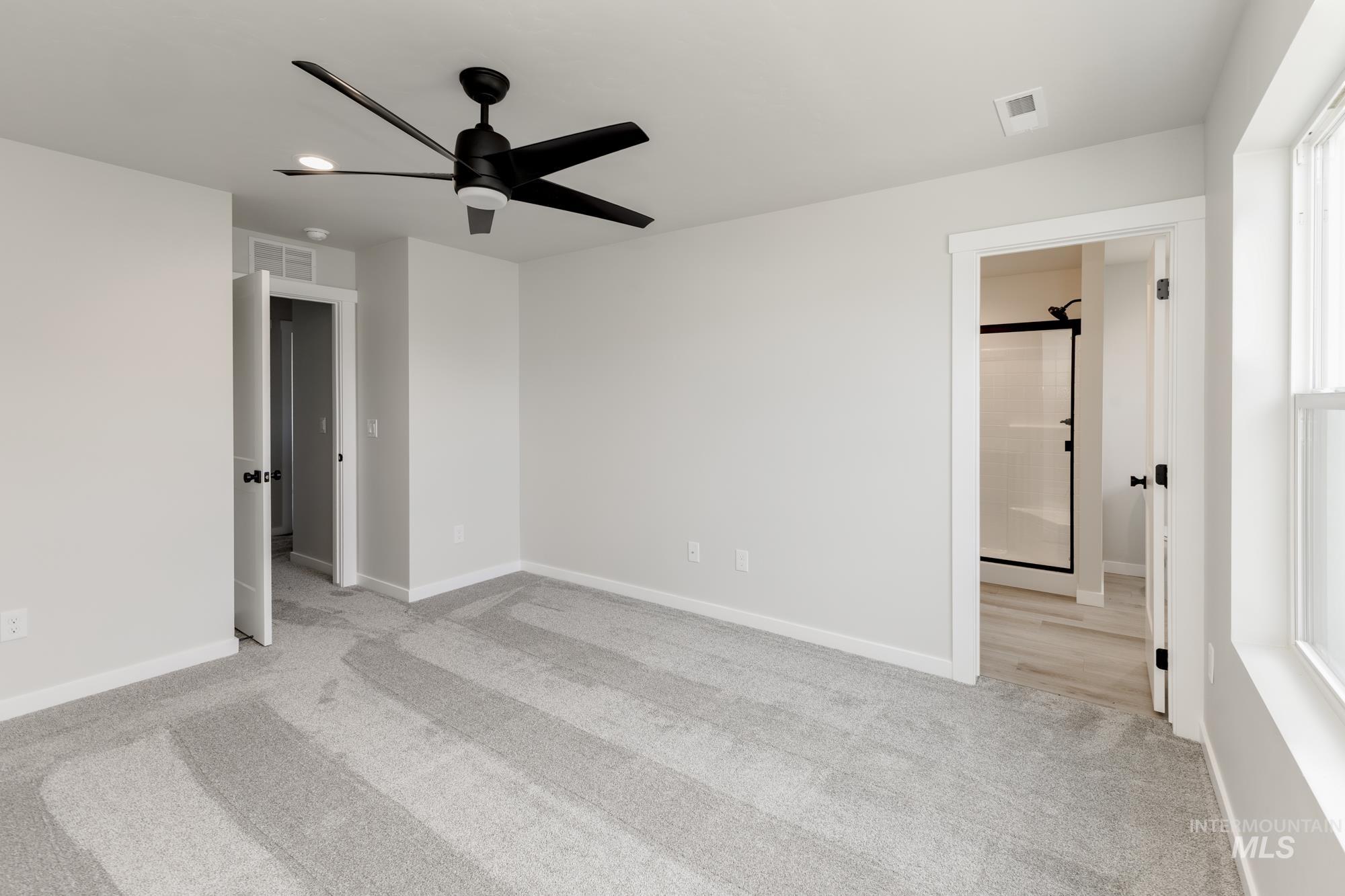 Unfurnished bedroom featuring light carpet, ceiling fan, and ensuite bathroom
