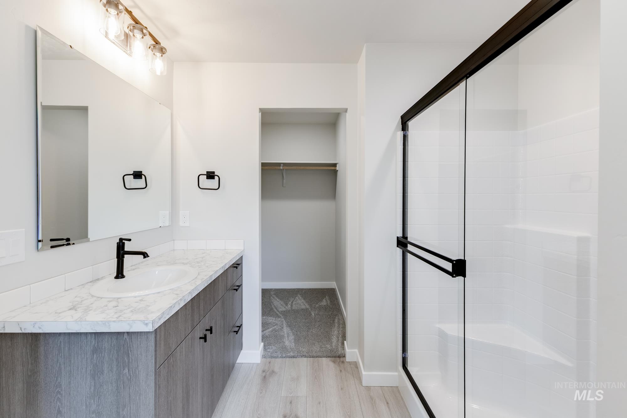 Bathroom featuring vanity, a walk in closet, light wood finished floors, and a shower stall