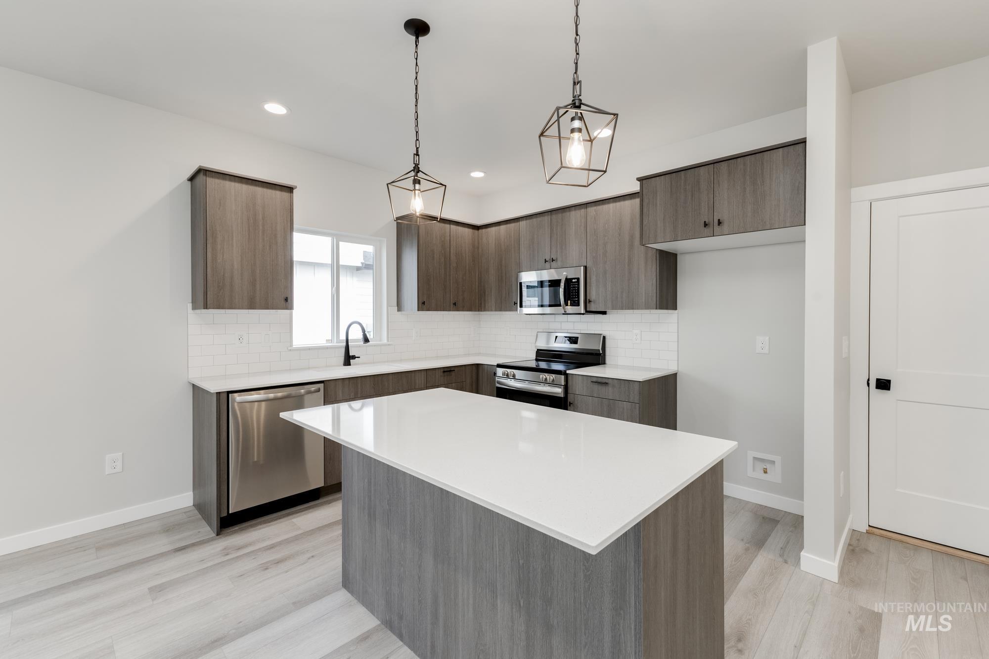 Kitchen featuring backsplash, stainless steel appliances, pendant lighting, a kitchen island, and light wood-style flooring