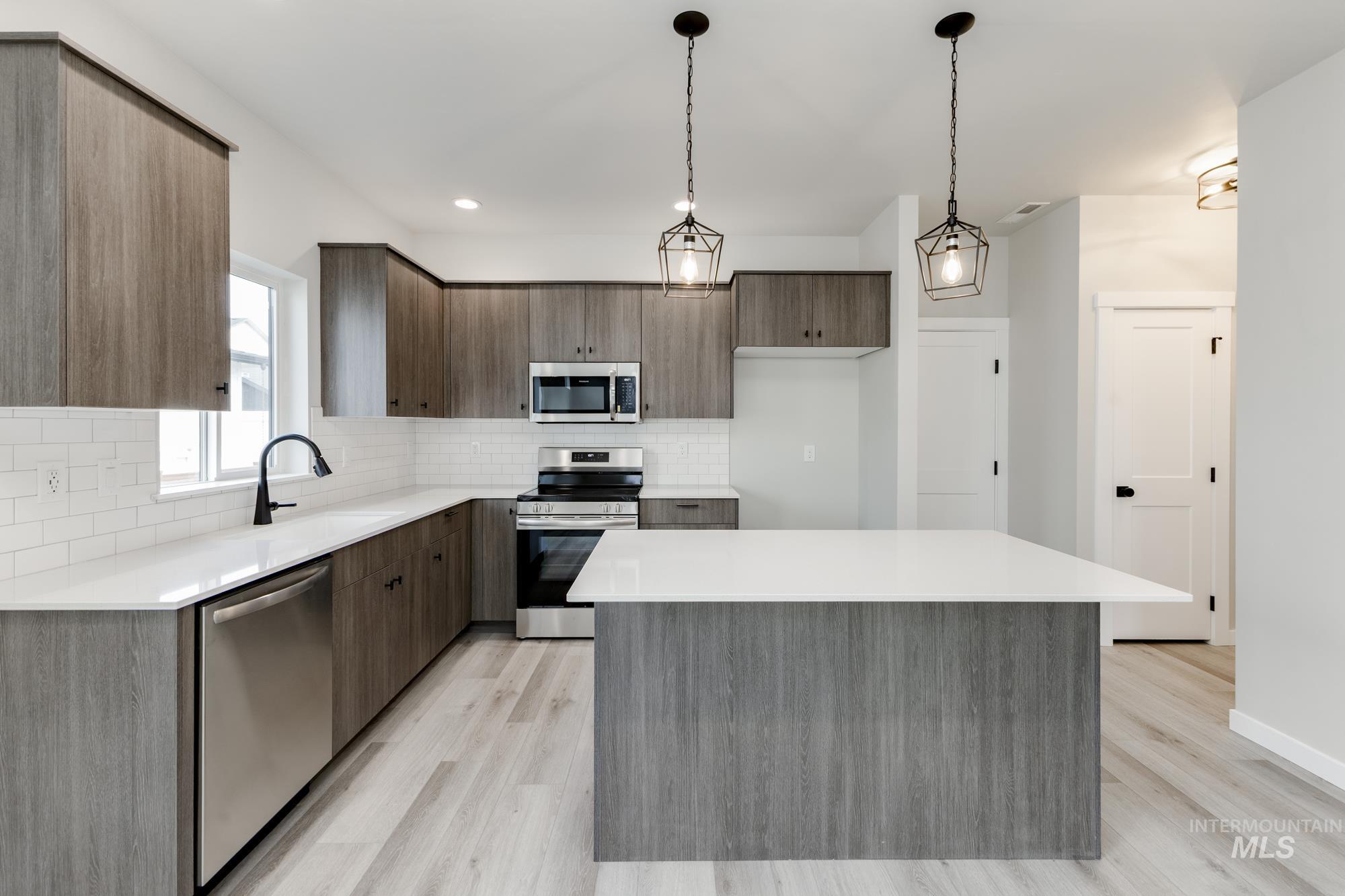 Kitchen with stainless steel appliances, a kitchen island, decorative backsplash, decorative light fixtures, and light wood finished floors