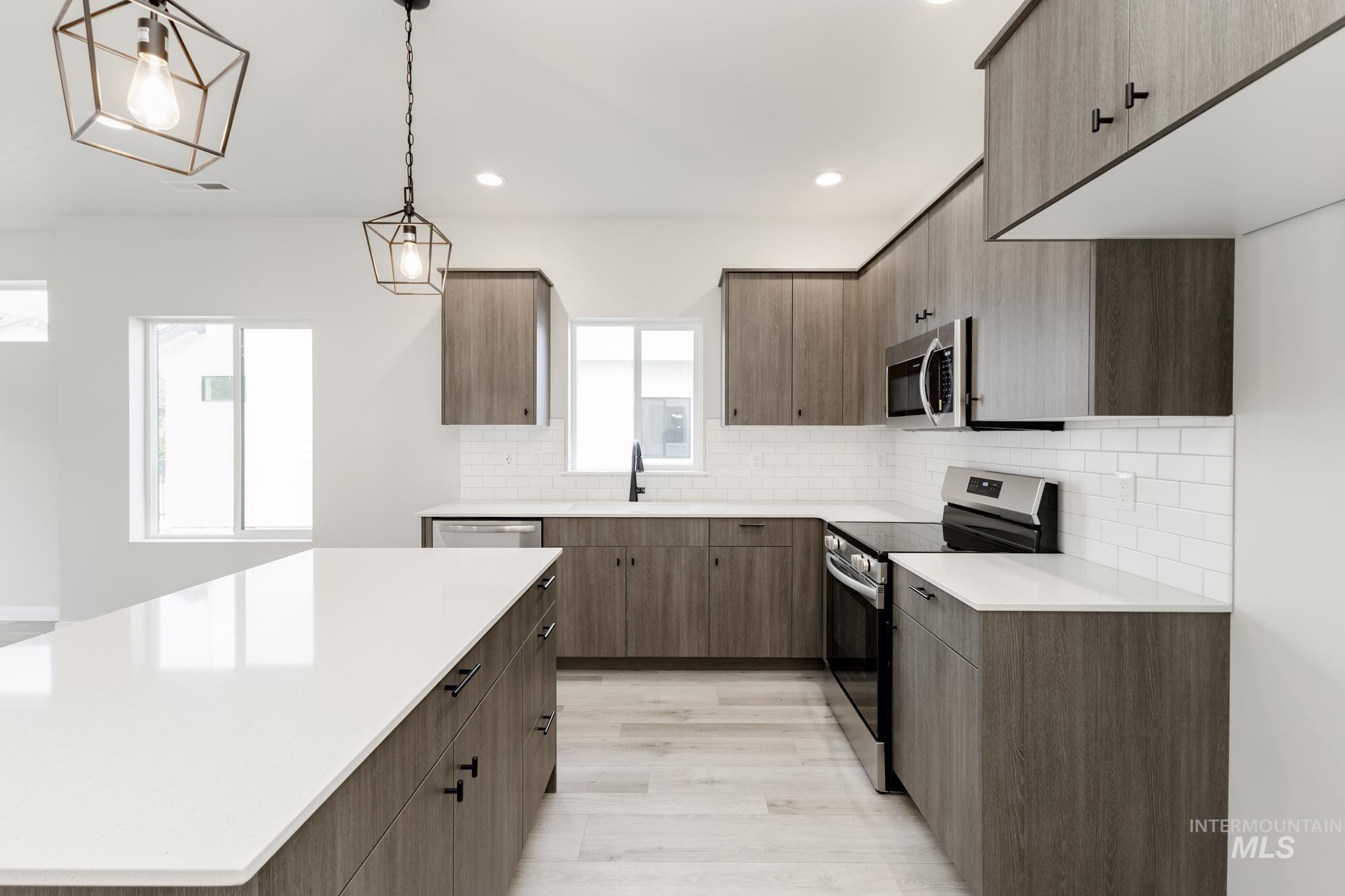 Kitchen with stainless steel appliances, tasteful backsplash, decorative light fixtures, light wood finished floors, and recessed lighting