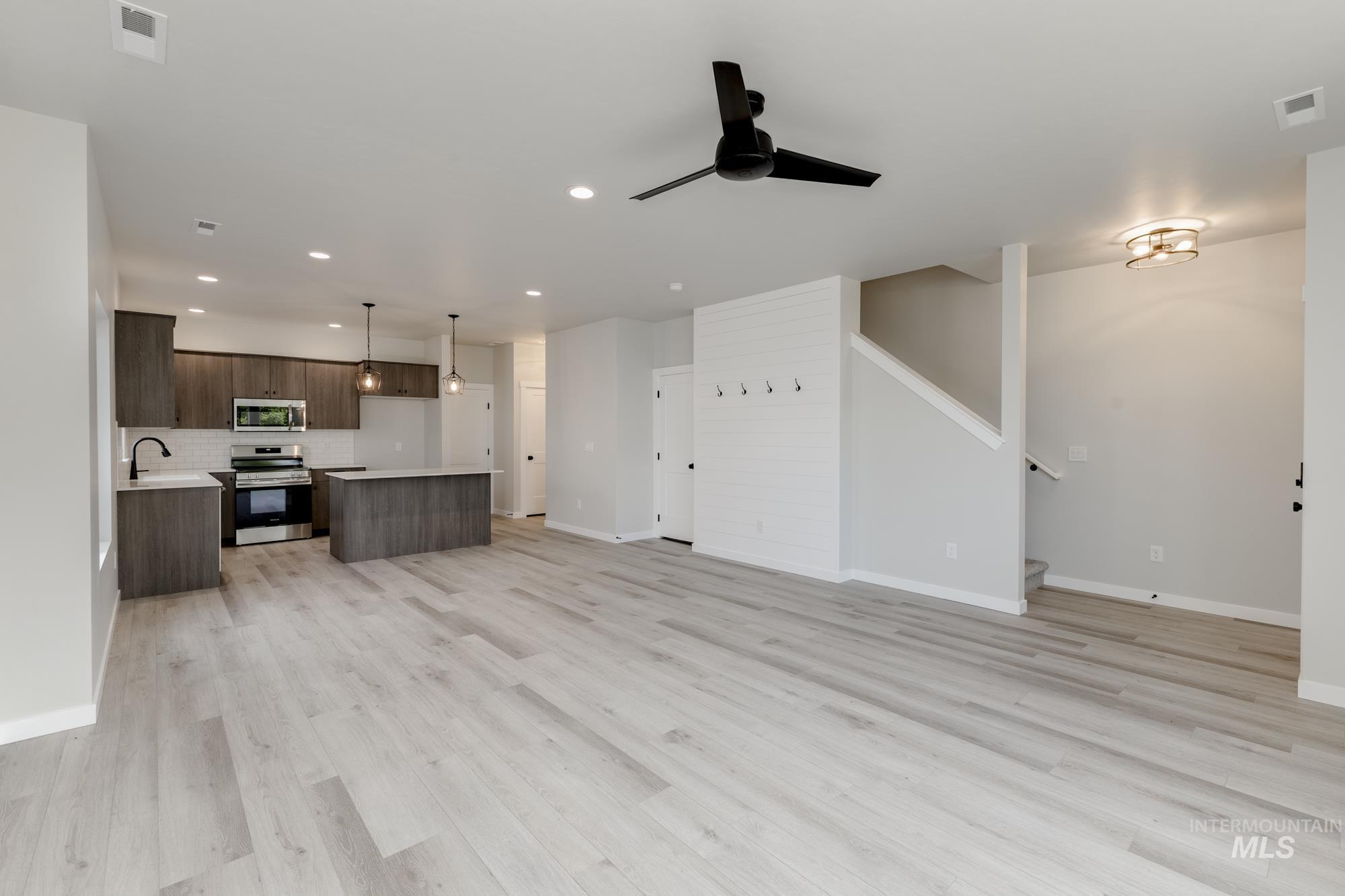 Unfurnished living room featuring ceiling fan, light wood finished floors, recessed lighting, and stairs