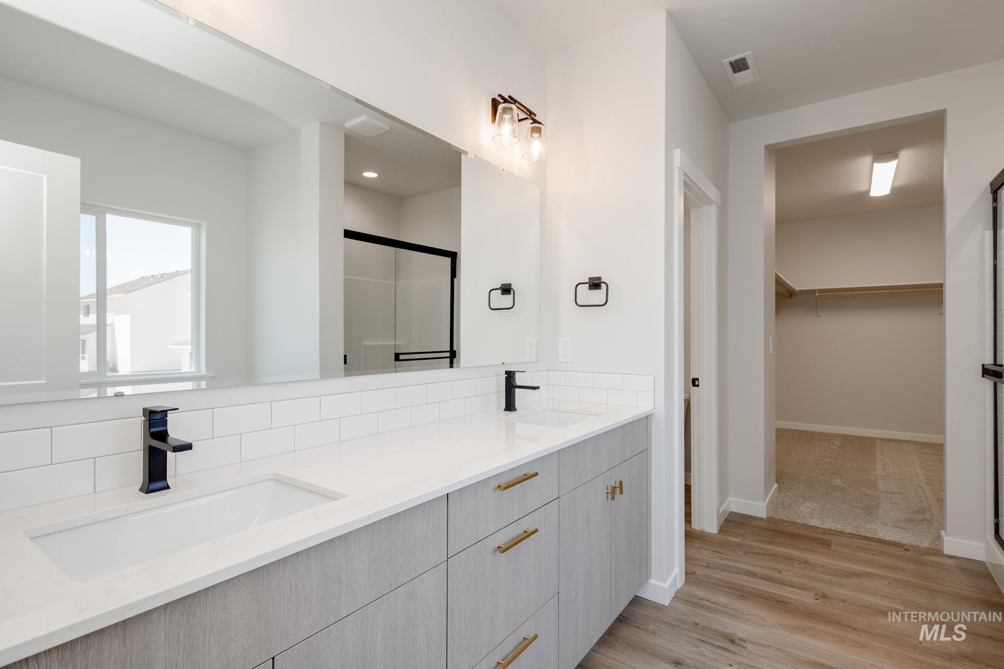 Full bath with a walk in closet, double vanity, a shower stall, wood finished floors, and backsplash