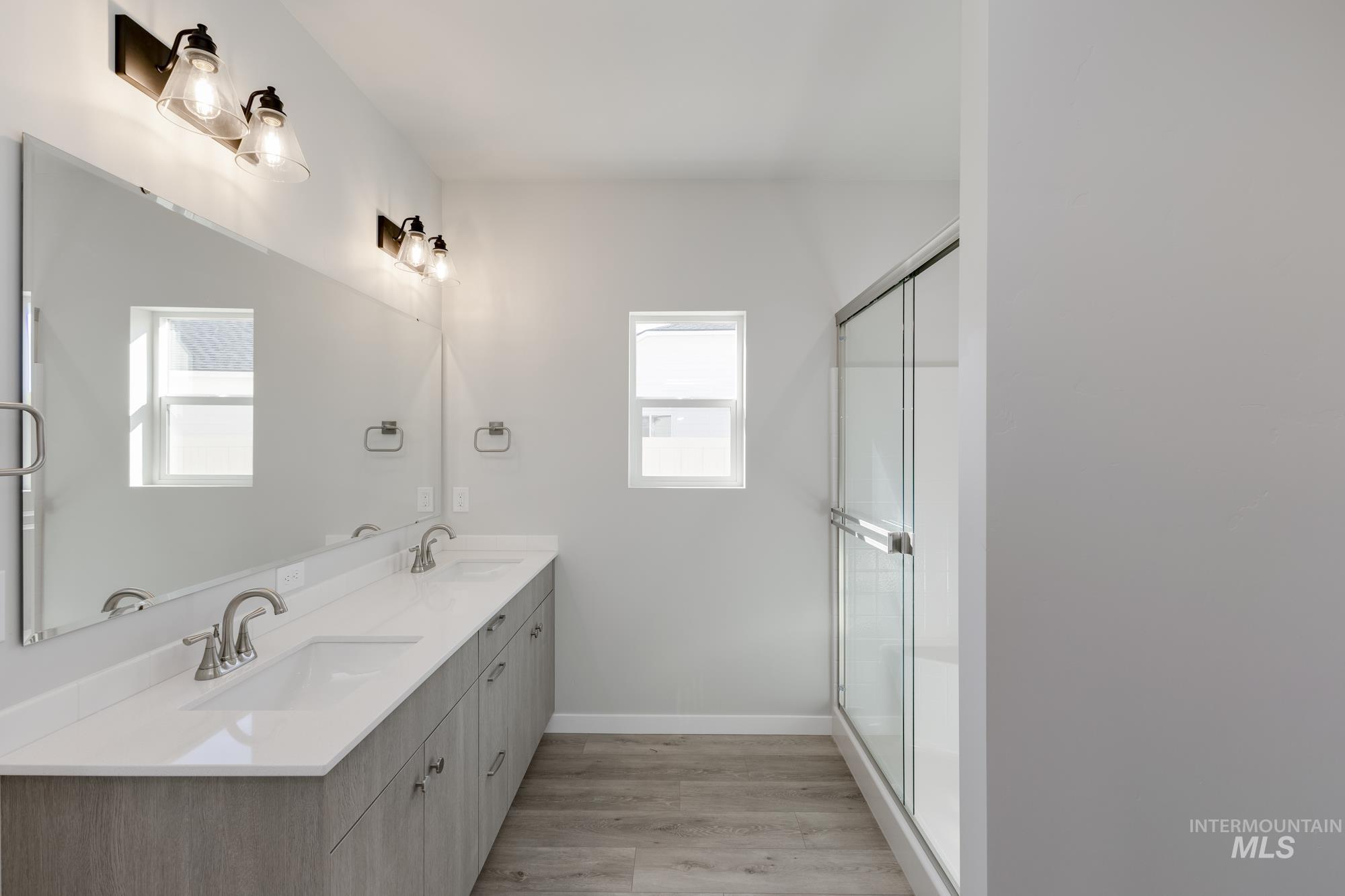 Full bathroom with wood finished floors, double vanity, and a shower with door