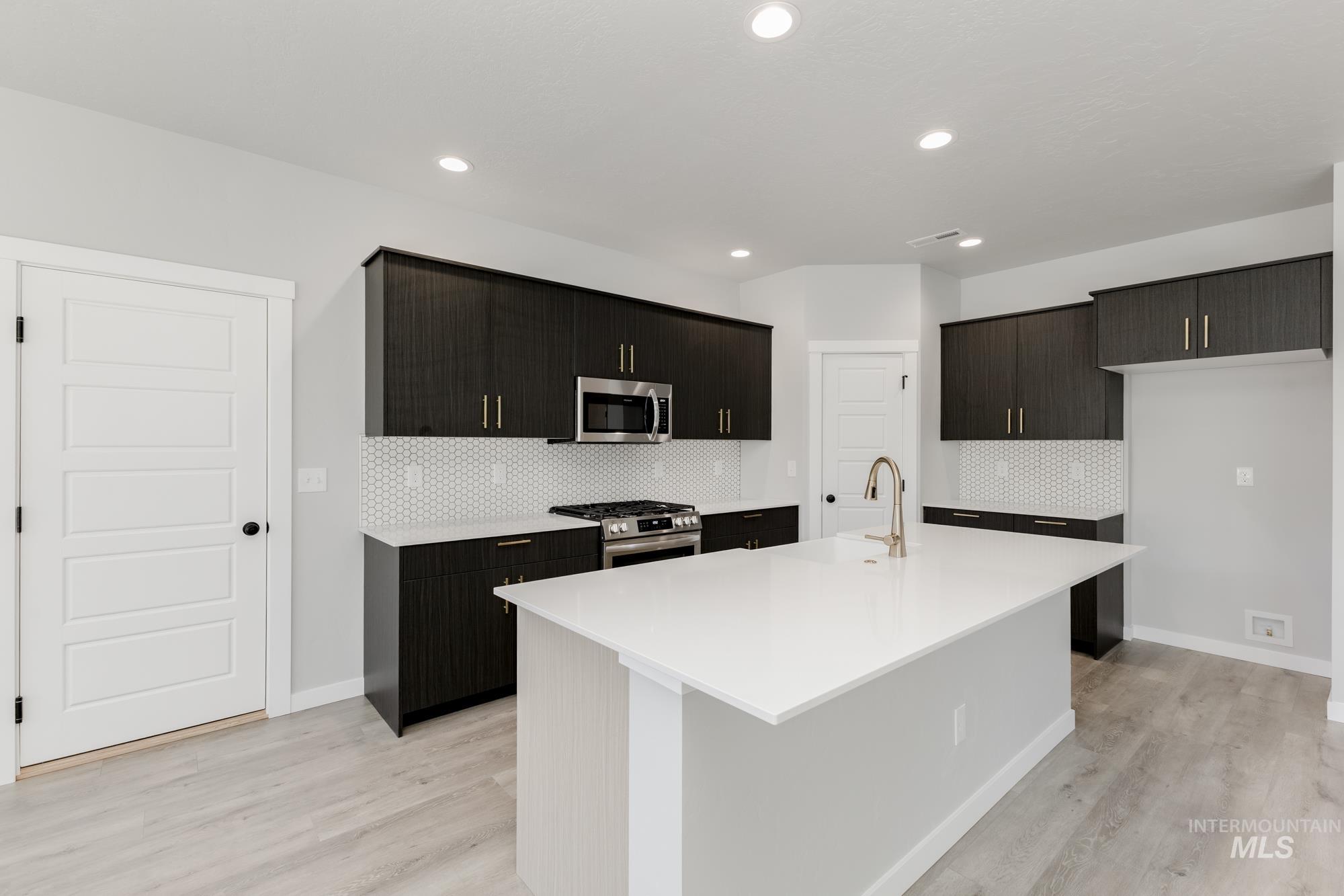 Kitchen with appliances with stainless steel finishes, light wood finished floors, decorative backsplash, a center island with sink, and light countertops