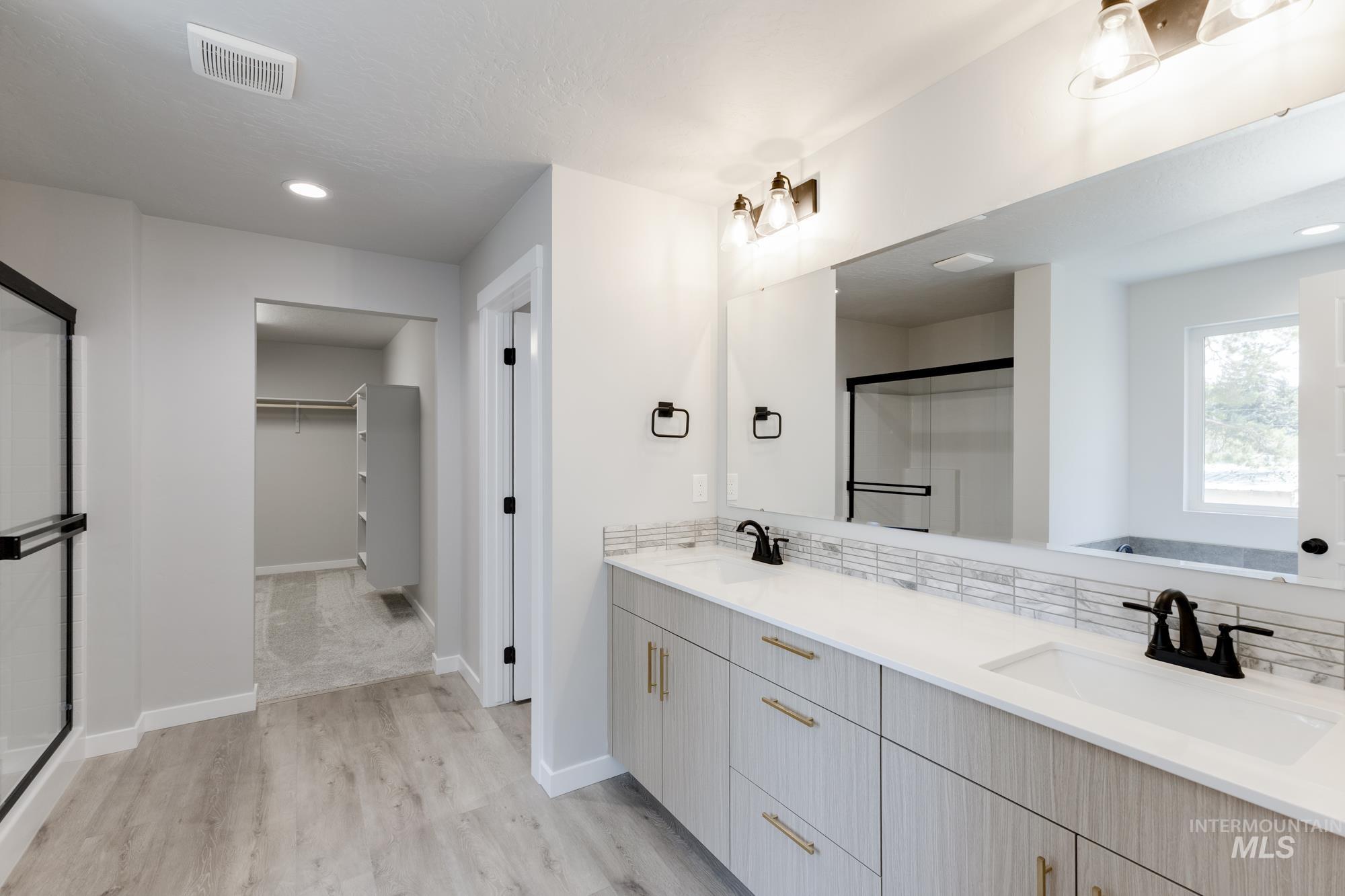 Bathroom with double vanity, a spacious closet, tasteful backsplash, a stall shower, and wood finished floors