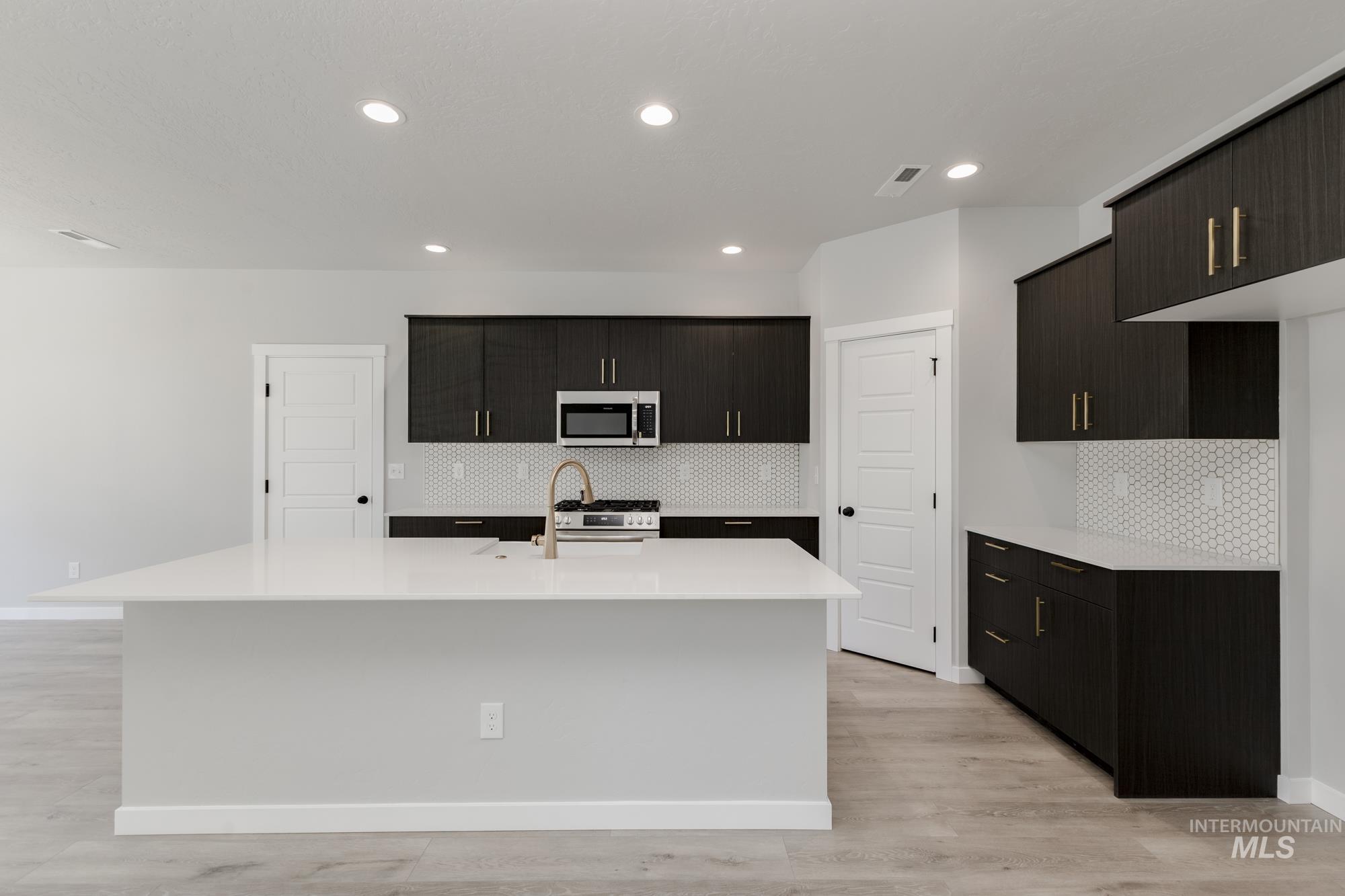 Kitchen featuring stainless steel appliances, a center island with sink, decorative backsplash, light countertops, and recessed lighting