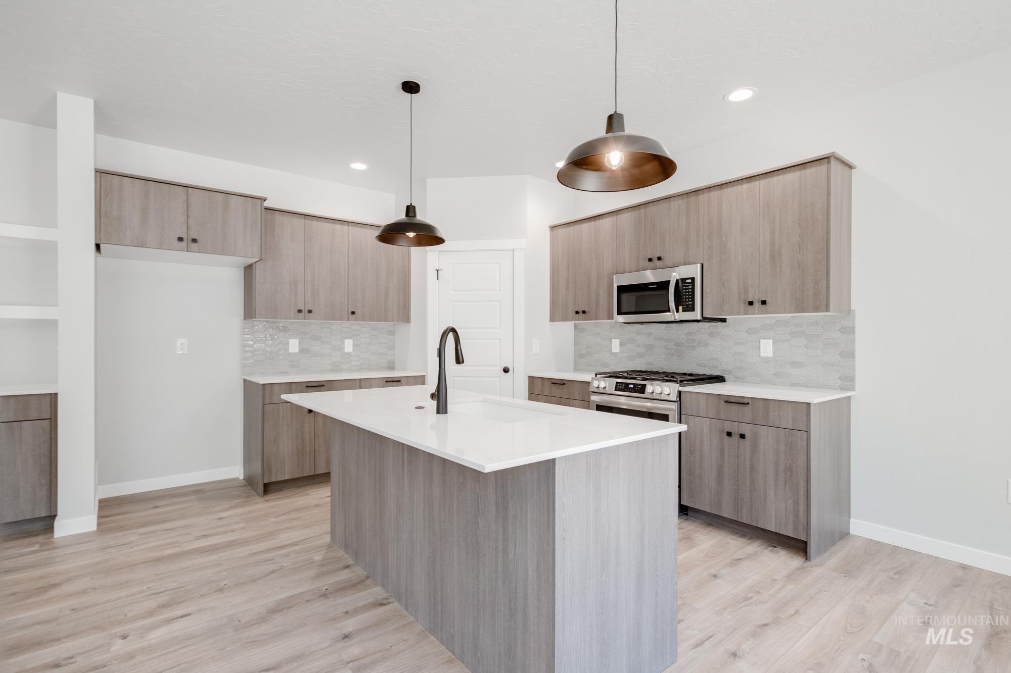 Kitchen featuring appliances with stainless steel finishes, modern cabinets, light countertops, tasteful backsplash, and light wood finished floors
