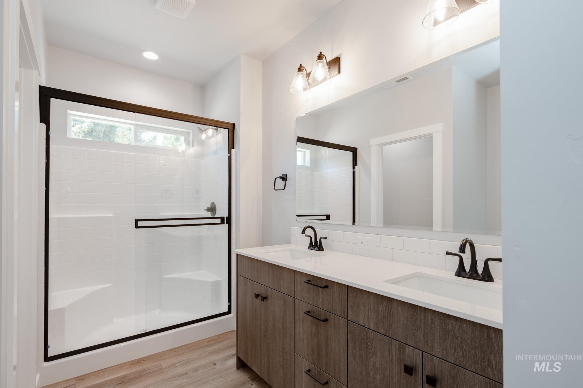 Full bath with double vanity, a shower stall, wood finished floors, and backsplash