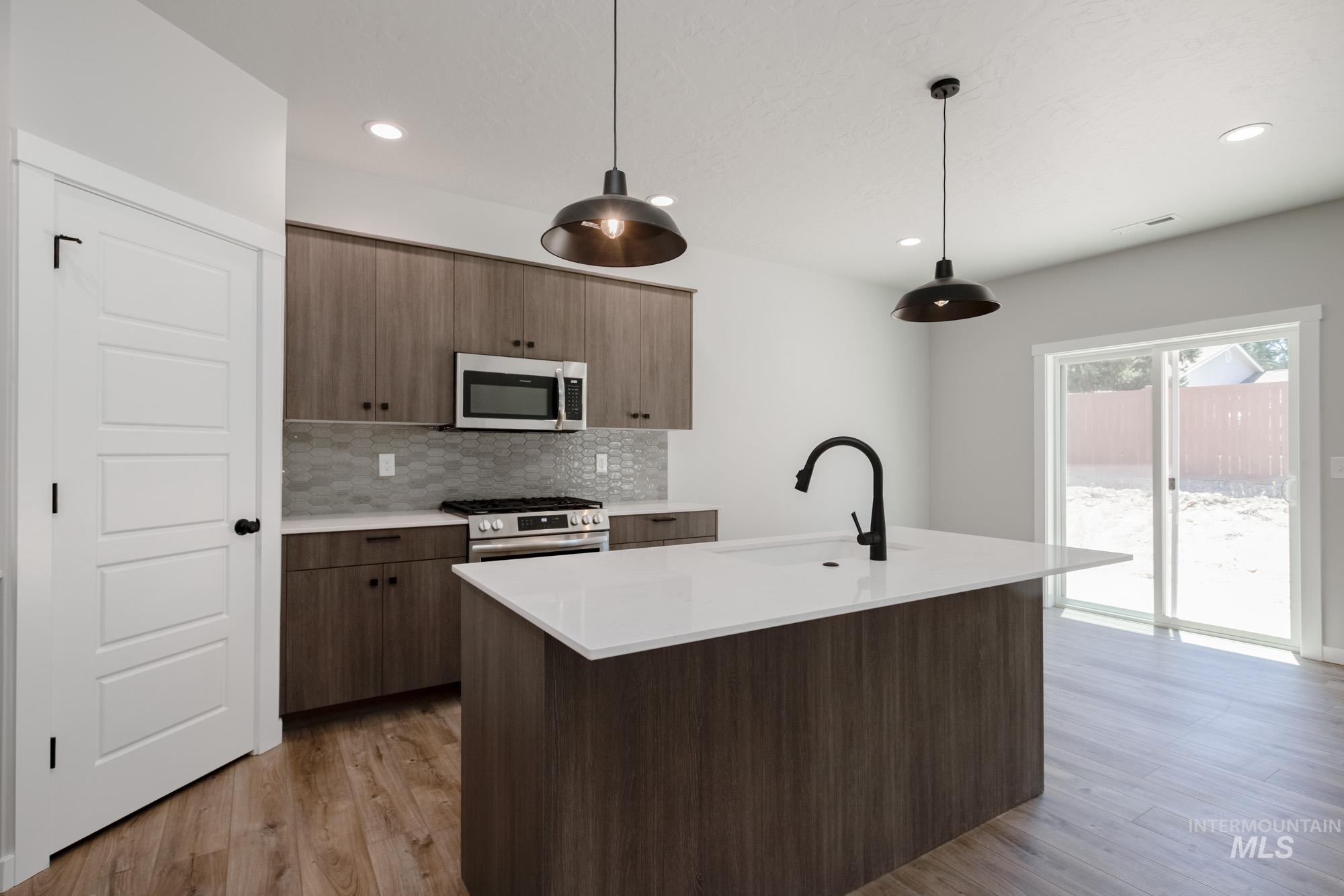 Kitchen with appliances with stainless steel finishes, light wood-style floors, light countertops, decorative backsplash, and pendant lighting