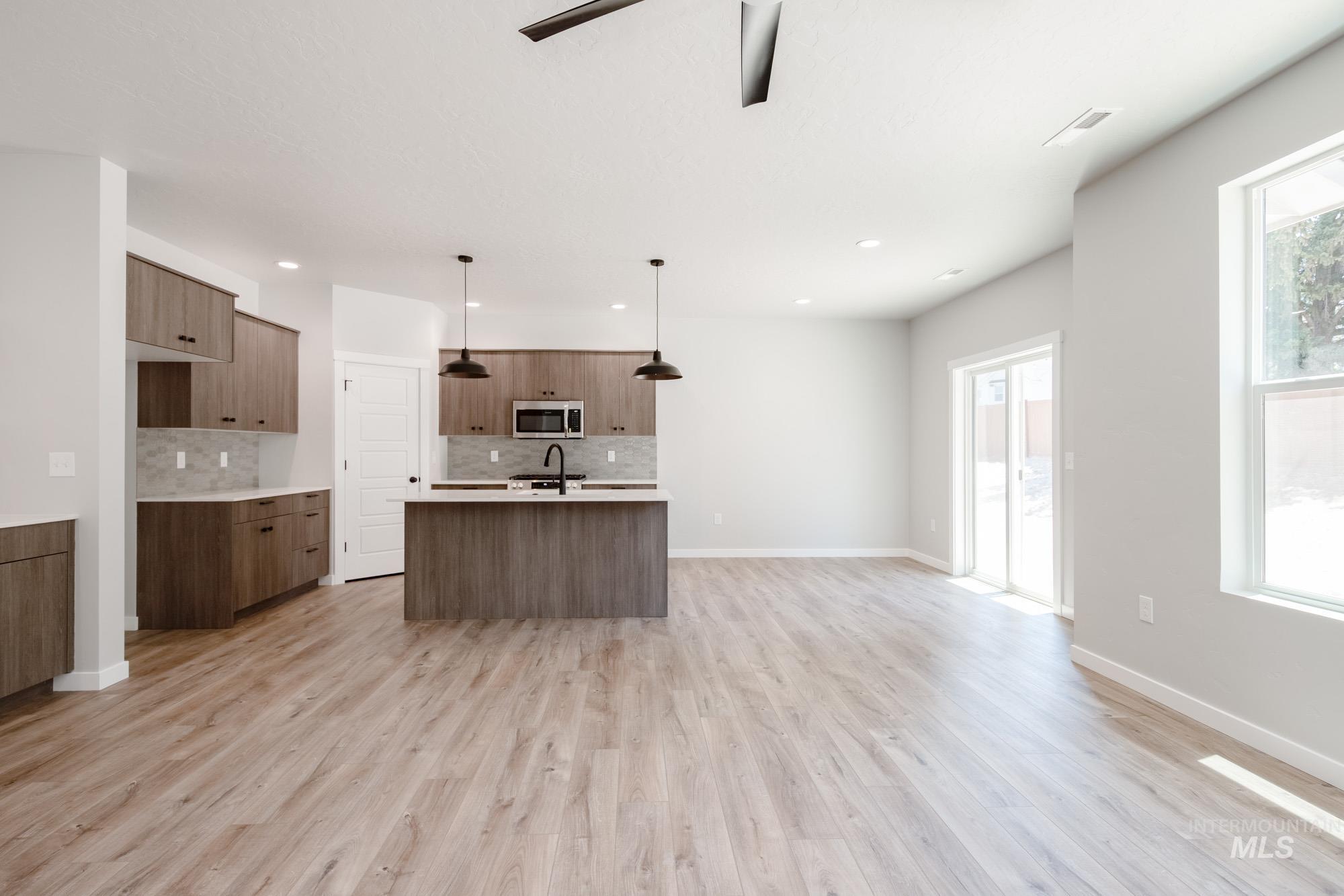 Kitchen with stainless steel microwave, modern cabinets, tasteful backsplash, open floor plan, and light wood-style flooring