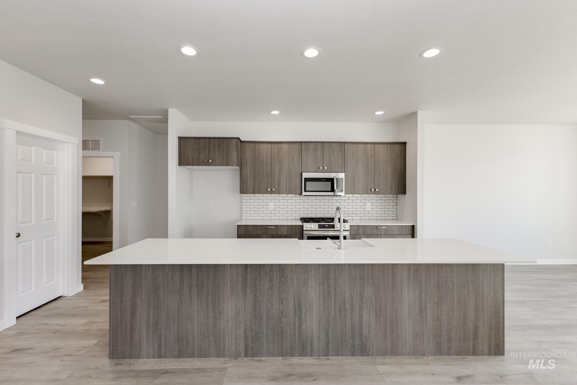 Kitchen with stainless steel appliances, a large island, light countertops, decorative backsplash, and recessed lighting