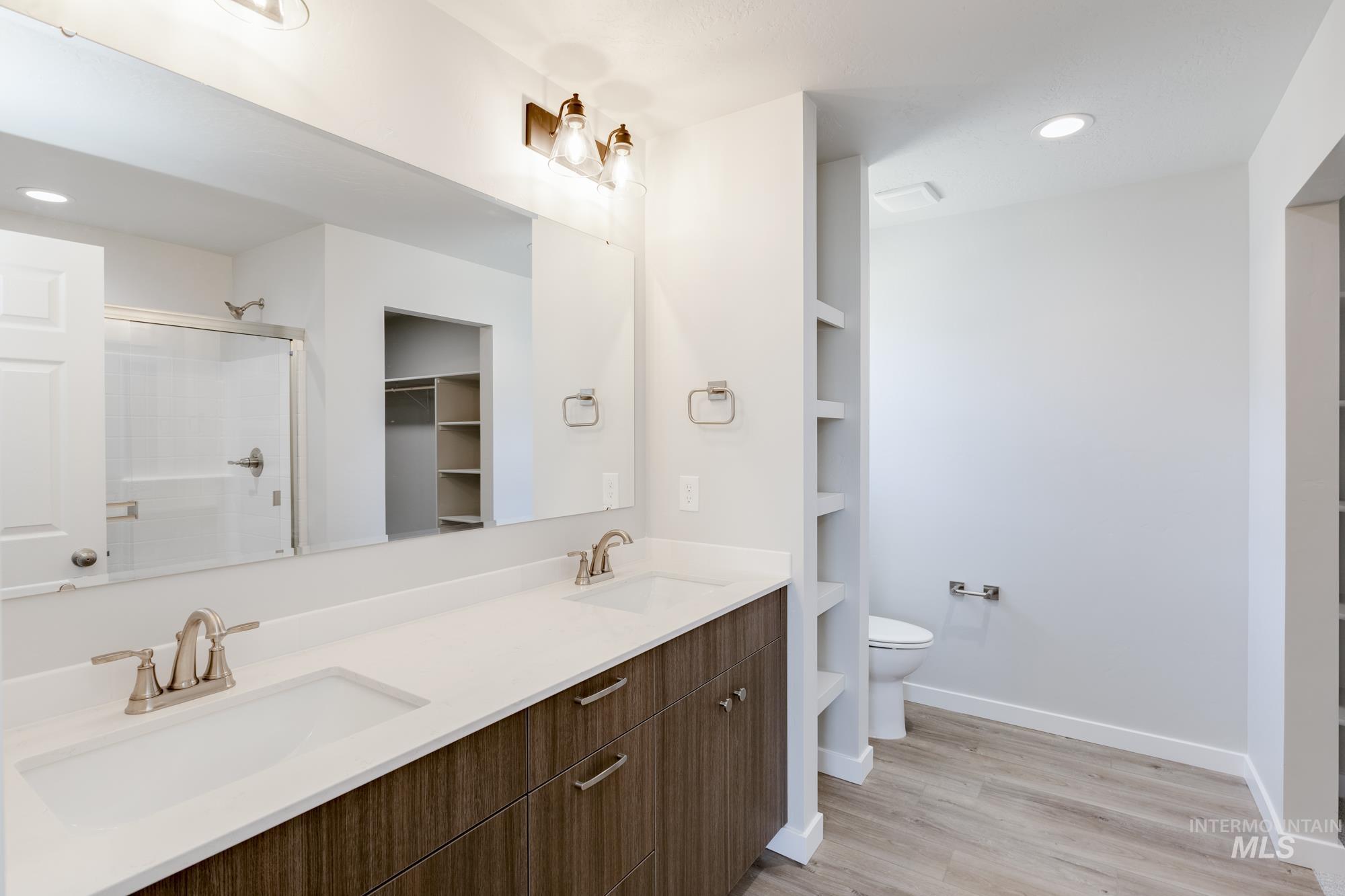 Bathroom featuring double vanity, a shower with shower door, wood finished floors, recessed lighting, and a spacious closet