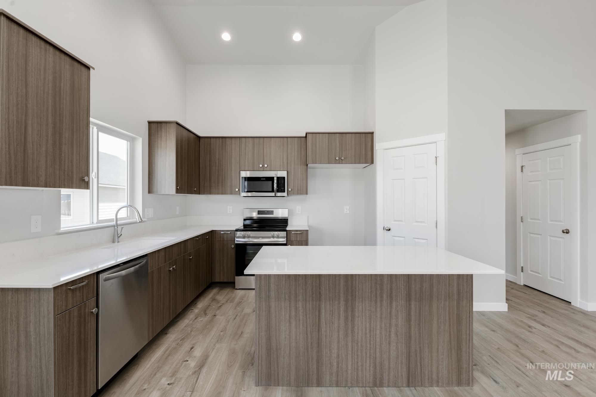 Kitchen with stainless steel appliances, a high ceiling, light wood-style flooring, light countertops, and a kitchen island