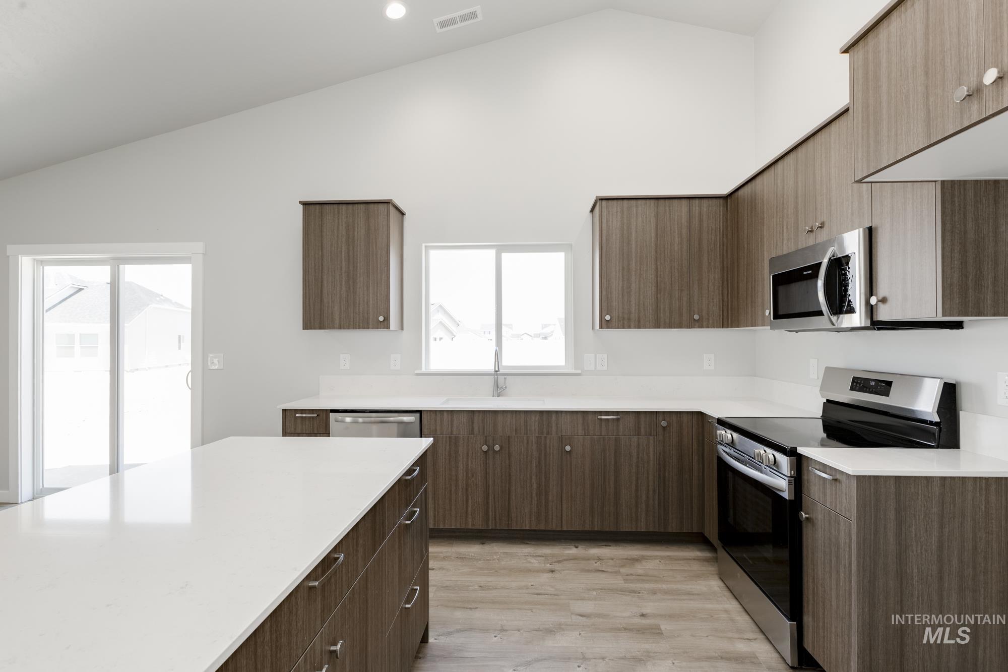 Kitchen with stainless steel appliances, high vaulted ceiling, light countertops, light wood-style flooring, and modern cabinets