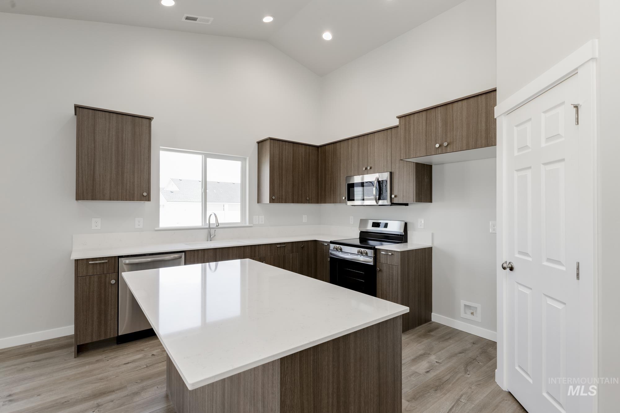Kitchen with appliances with stainless steel finishes, high vaulted ceiling, light countertops, a kitchen island, and light wood-style flooring