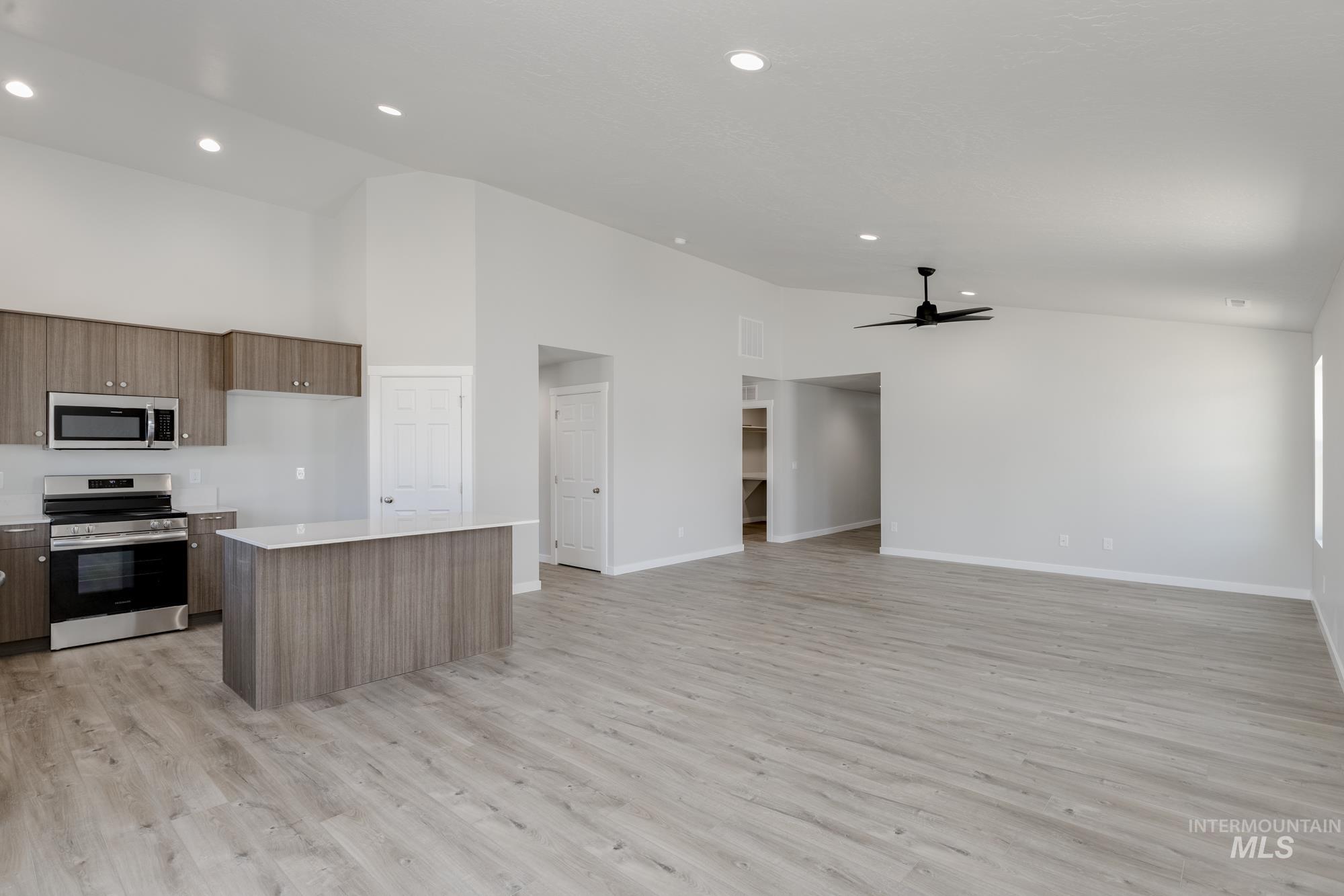 Kitchen featuring appliances with stainless steel finishes, light countertops, a center island, ceiling fan, and light wood-style flooring