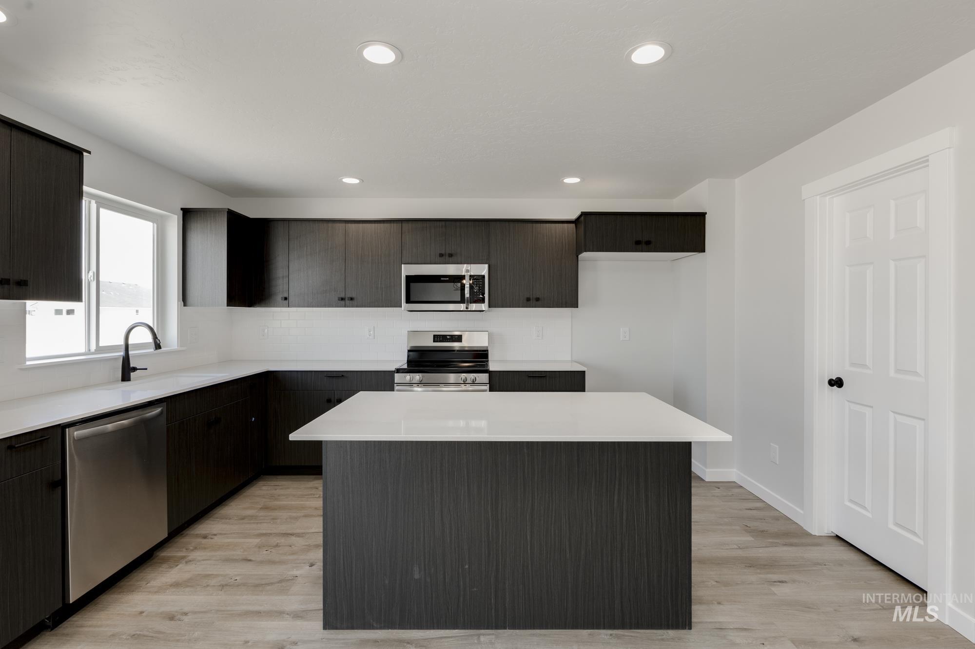 Kitchen featuring appliances with stainless steel finishes, a center island, light countertops, light wood-style floors, and recessed lighting