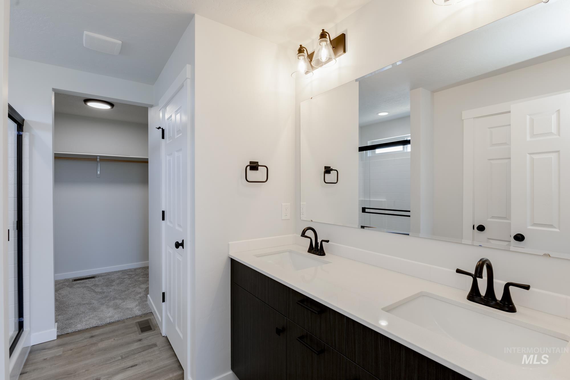 Full bath with wood finished floors, double vanity, a spacious closet, and a shower with door
