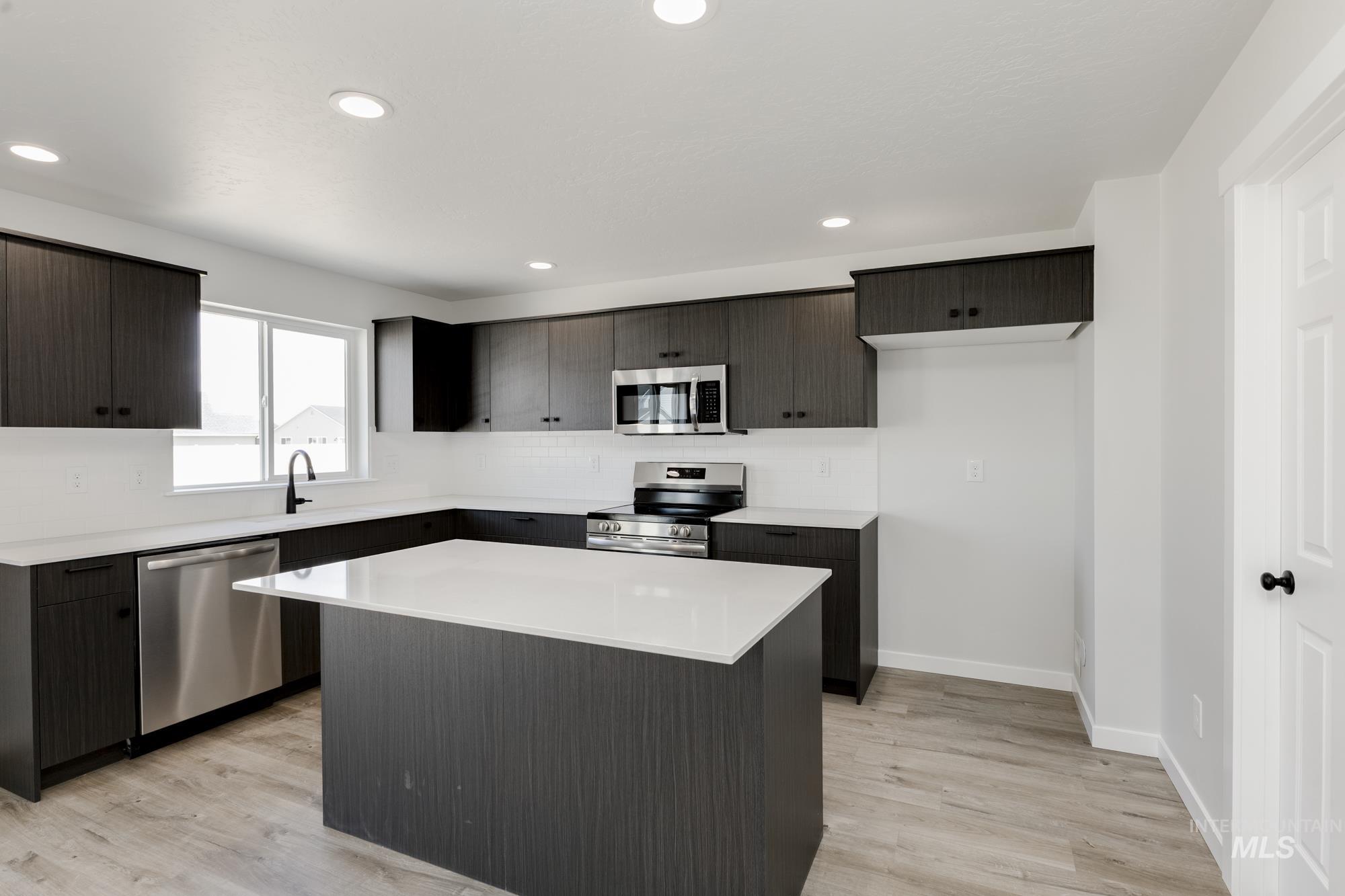 Kitchen with stainless steel appliances, a kitchen island, light countertops, light wood-style floors, and recessed lighting