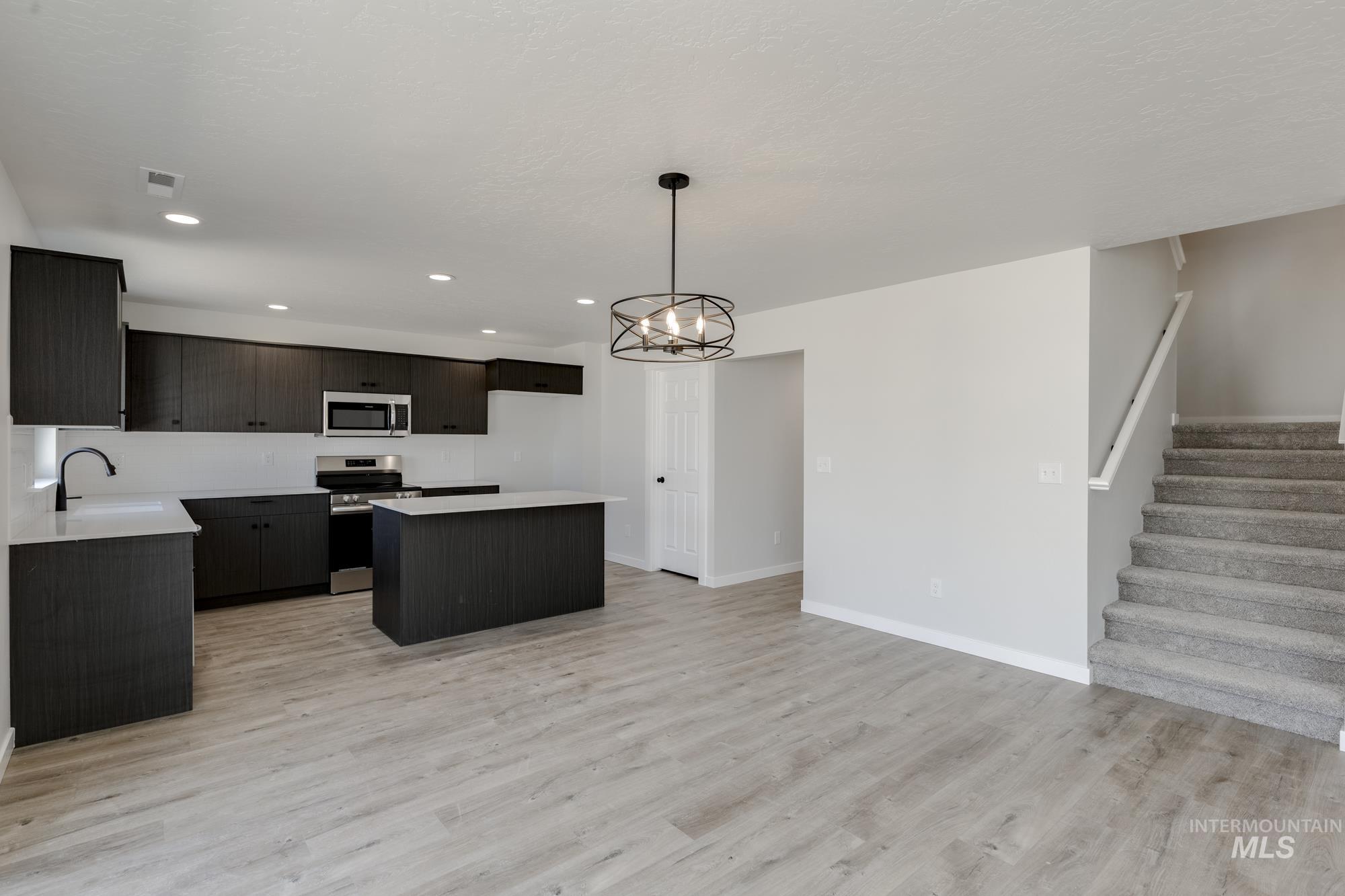 Kitchen with stainless steel appliances, a kitchen island, light wood-style flooring, recessed lighting, and a chandelier
