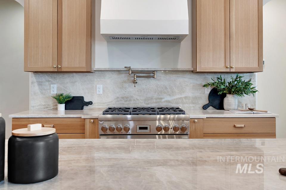 Kitchen with tasteful backsplash, wall chimney exhaust hood, and light brown cabinetry