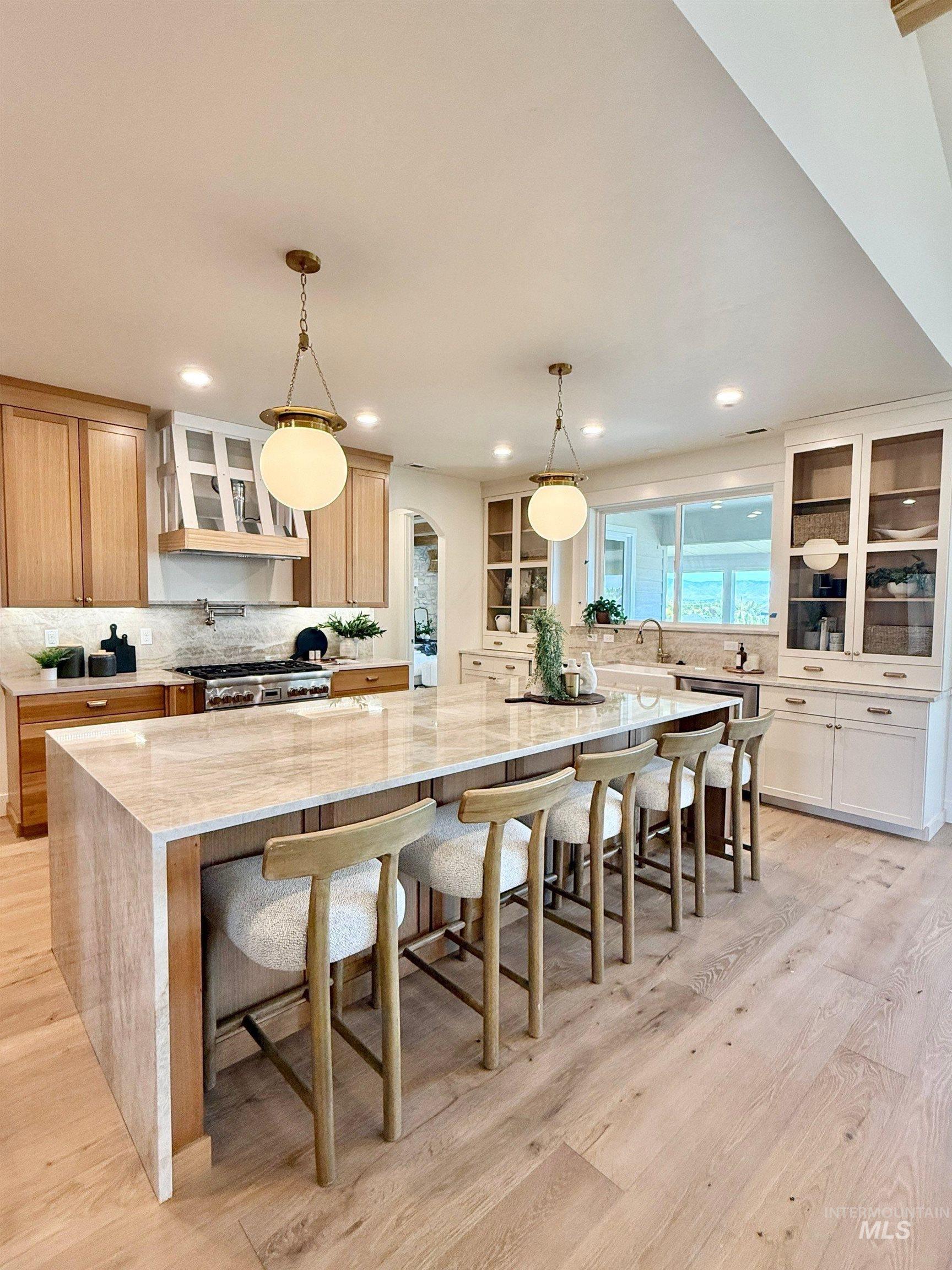 Kitchen with glass insert cabinets, backsplash, light stone counters, a spacious island, and a breakfast bar