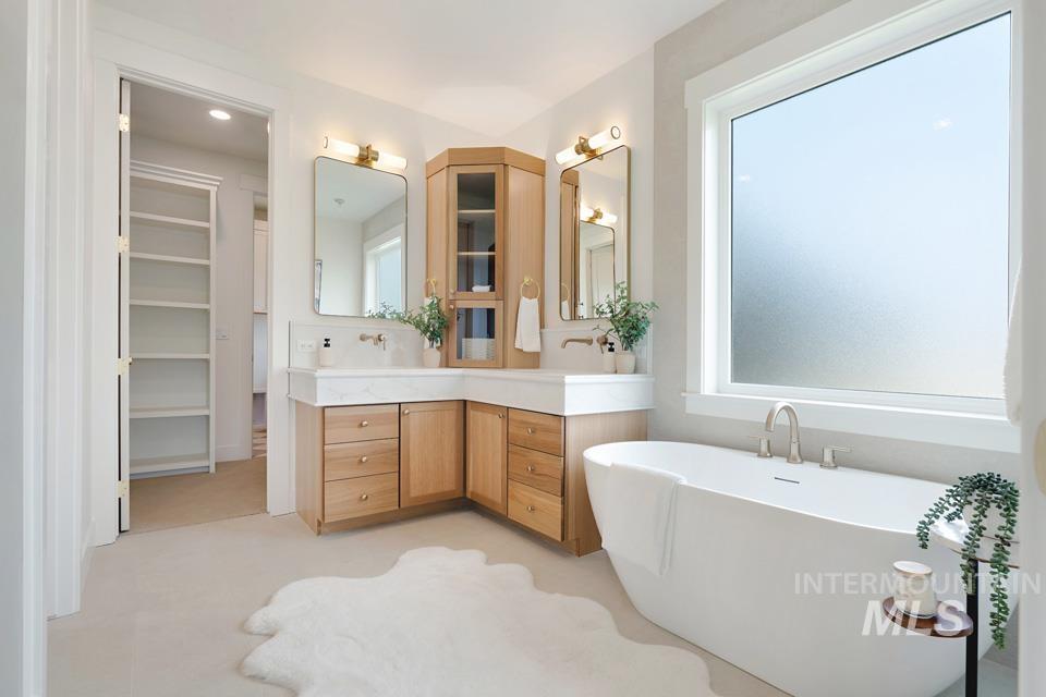 Bathroom with double vanity, a freestanding bath, plenty of natural light, and a walk in closet