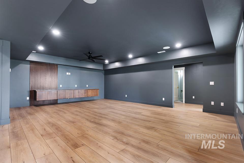 Unfurnished living room with a tray ceiling, a ceiling fan, light wood-style flooring, and recessed lighting