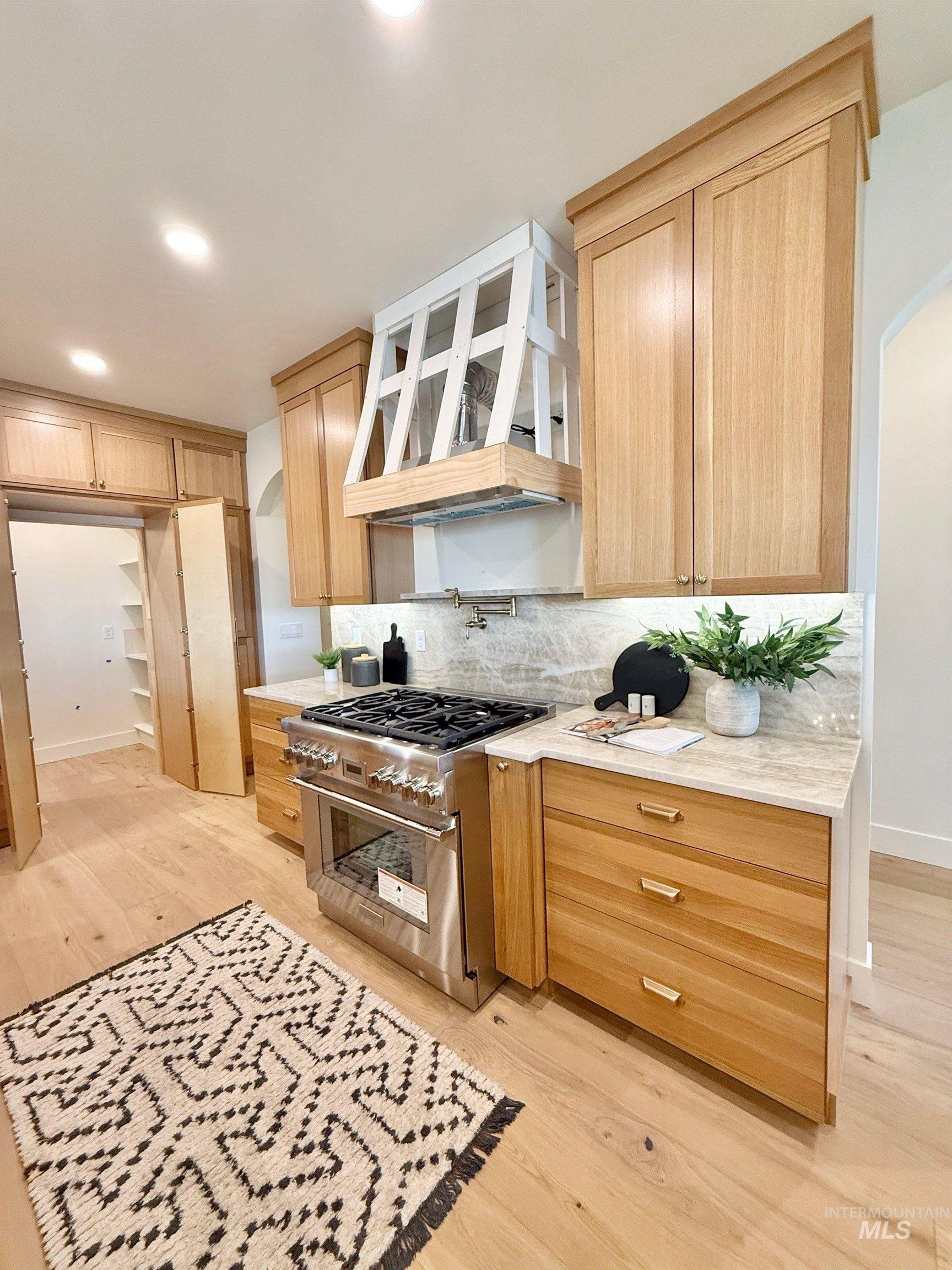 Kitchen with arched walkways, decorative backsplash, light wood-style flooring, high end range, and recessed lighting