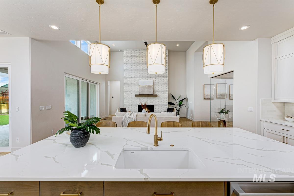 Kitchen with a center island with sink, light stone counters, hanging light fixtures, a fireplace, and open floor plan