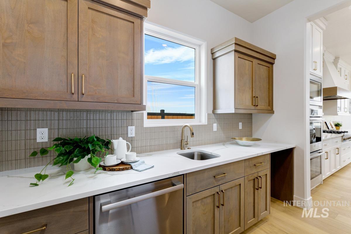 Kitchen featuring appliances with stainless steel finishes, decorative backsplash, light stone countertops, custom exhaust hood, and light wood finished floors