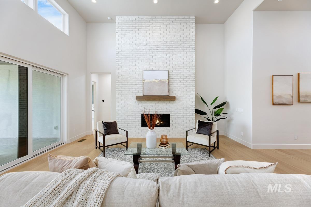 Living room featuring a brick fireplace, light wood-style flooring, a high ceiling, and recessed lighting