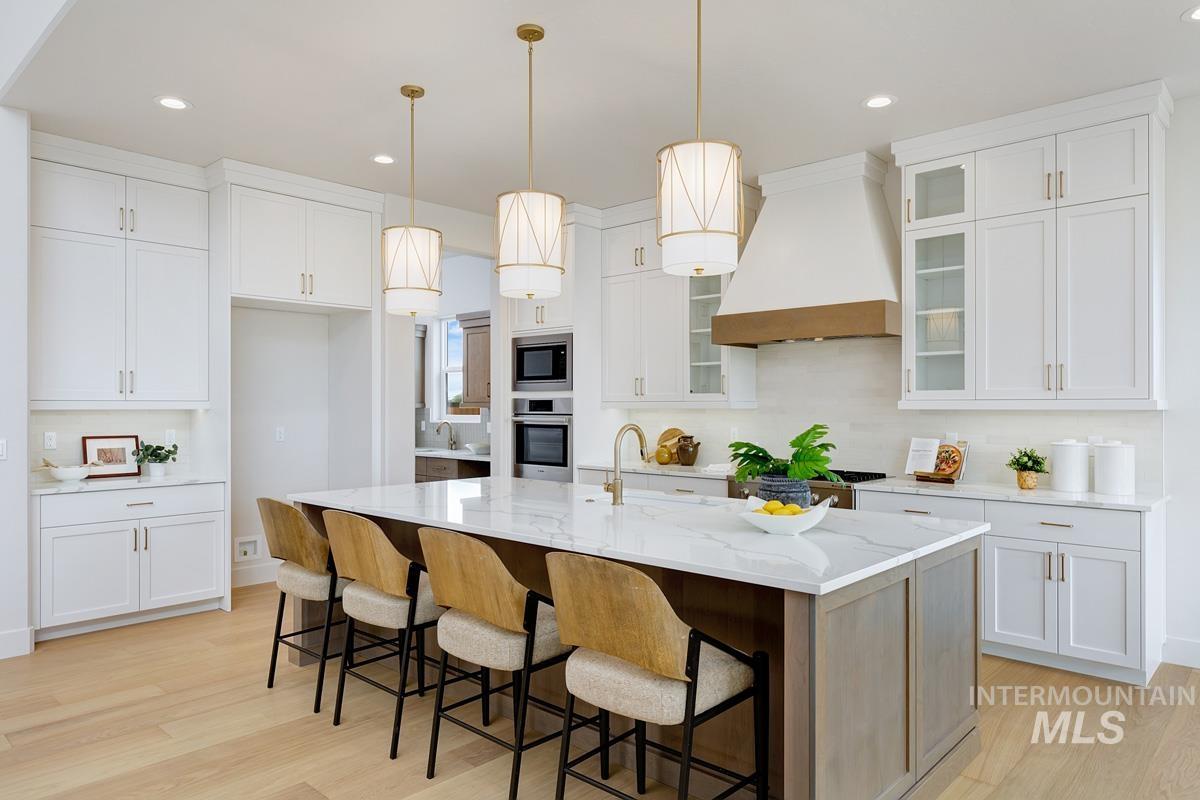 Kitchen featuring decorative light fixtures, white cabinetry, light wood-style floors, custom exhaust hood, and a breakfast bar area