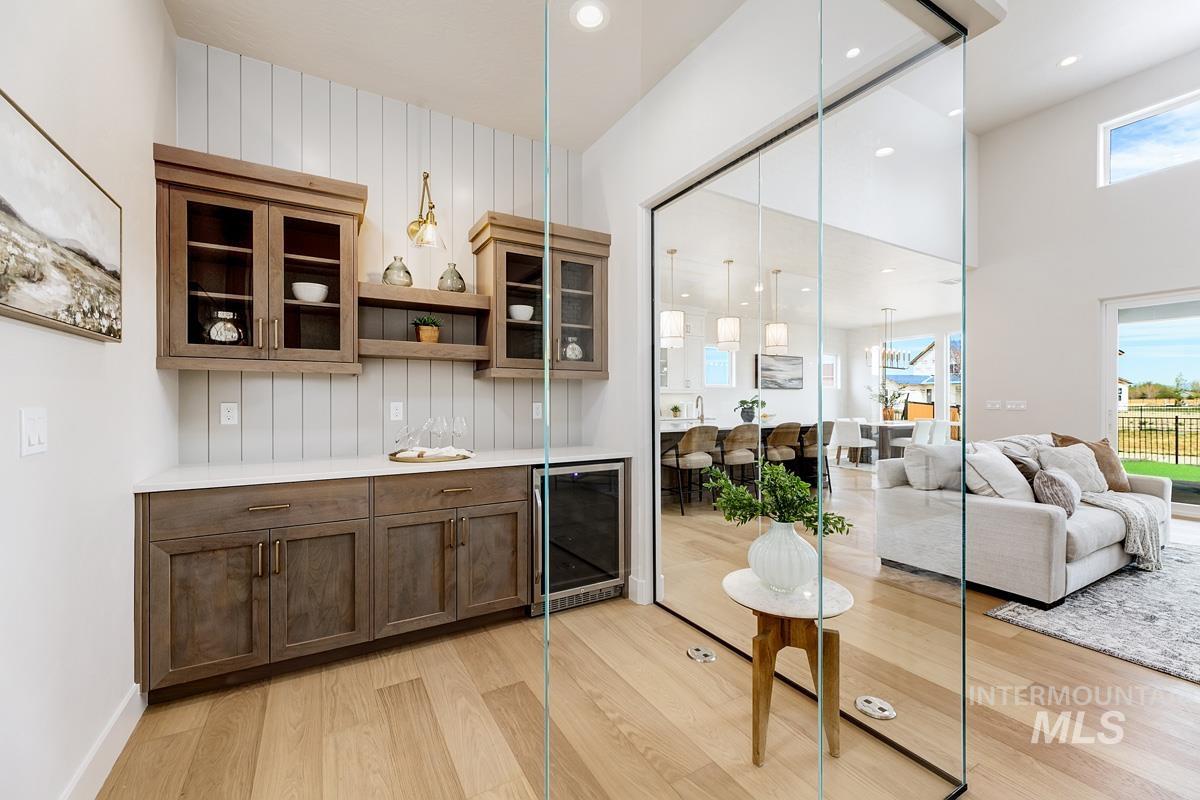 Bar area with glass insert cabinets, open shelves, beverage cooler, decorative light fixtures, and light wood-type flooring