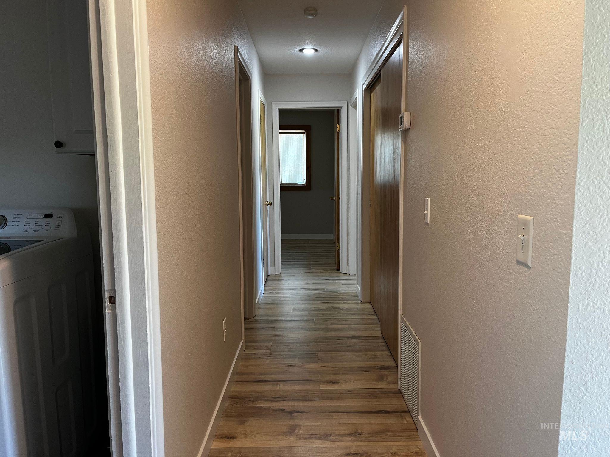 Hall with washer / dryer, dark wood-style flooring, and a textured wall