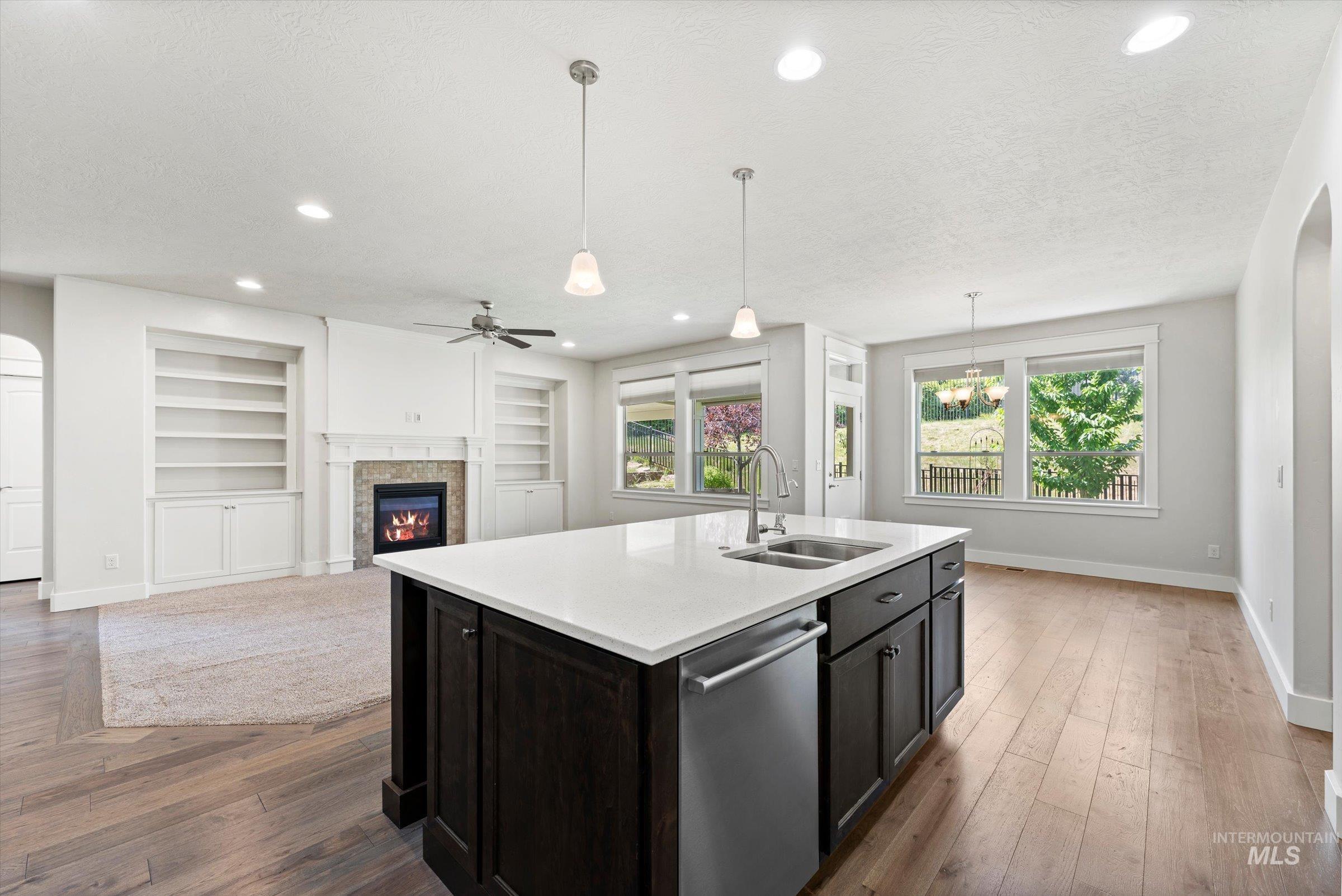 Kitchen featuring stainless steel dishwasher, a glass covered fireplace, light countertops, built in shelves, and a textured ceiling
