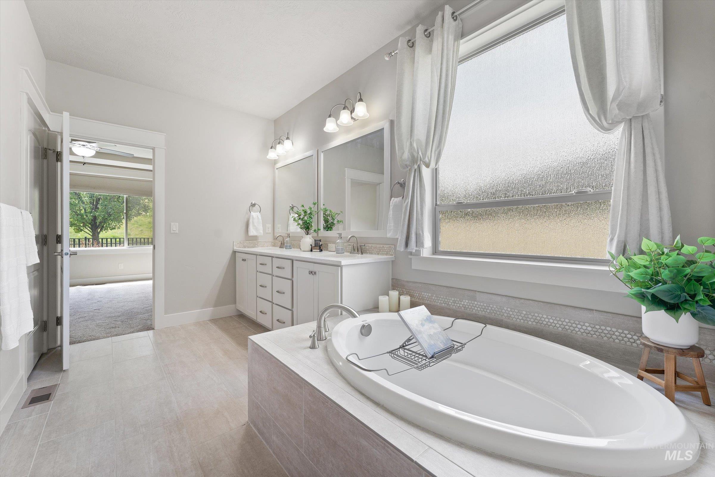 Full bath with double vanity, a bath, a ceiling fan, and light tile patterned floors